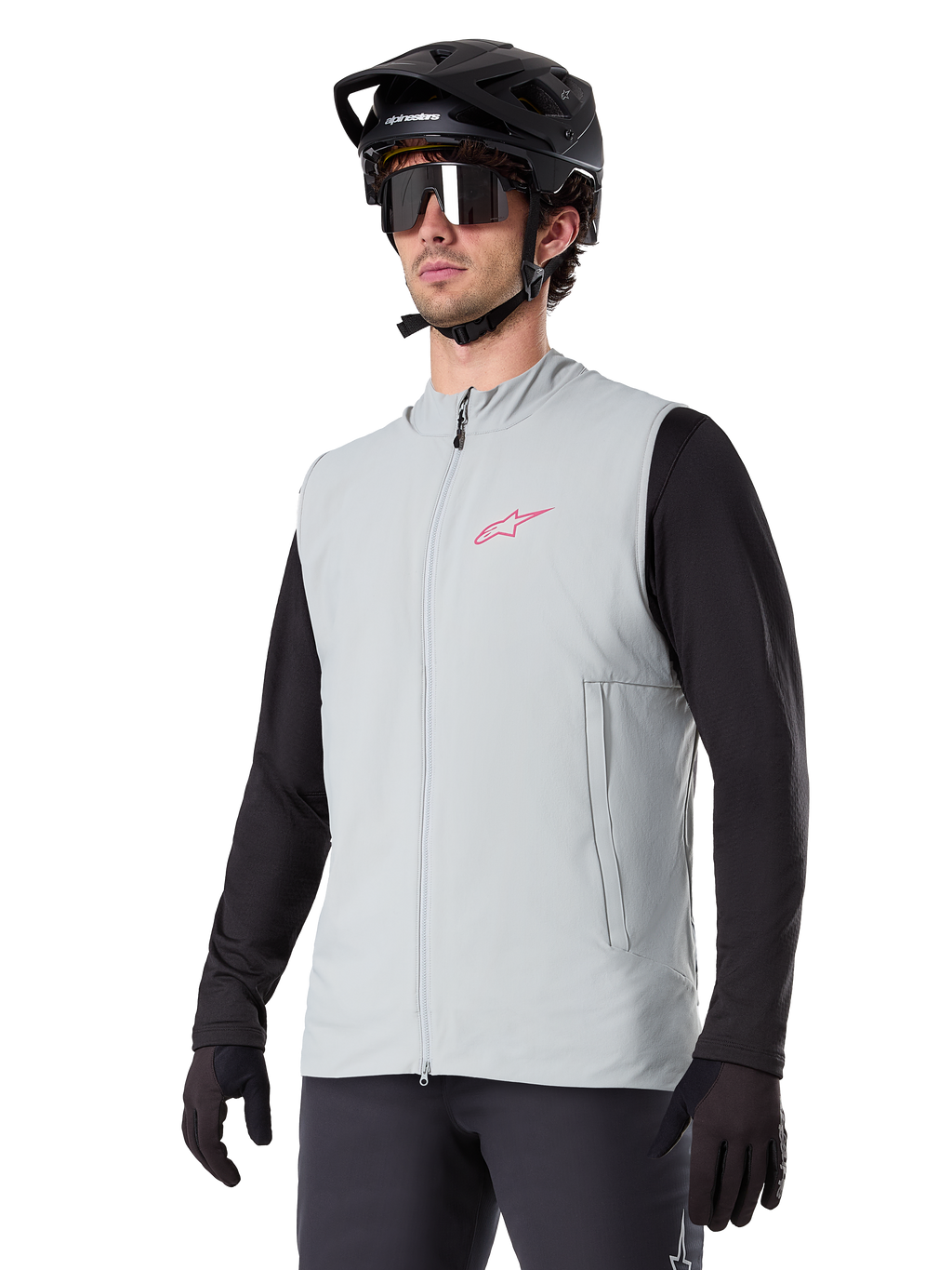 Alpinestars A-Dura Thermal Vest, titaniumgrå, isoleret cykelvest, båret over en sort langærmet trøje med sort mountainbikehjelm og handsker, med pink logo på brystet og lodrette sidelommer med lynlås