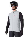 Alpinestars A-Dura Thermal Vest, titaniumgrå, isoleret cykelvest, båret over en sort langærmet trøje med sort mountainbikehjelm og handsker, med pink logo på brystet og lodrette sidelommer med lynlås