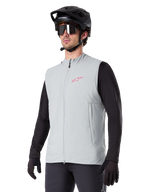 Alpinestars A-Dura Thermal Vest, titaniumgrå, isoleret cykelvest, båret over en sort langærmet trøje med sort mountainbikehjelm og handsker, med pink logo på brystet og lodrette sidelommer med lynlås