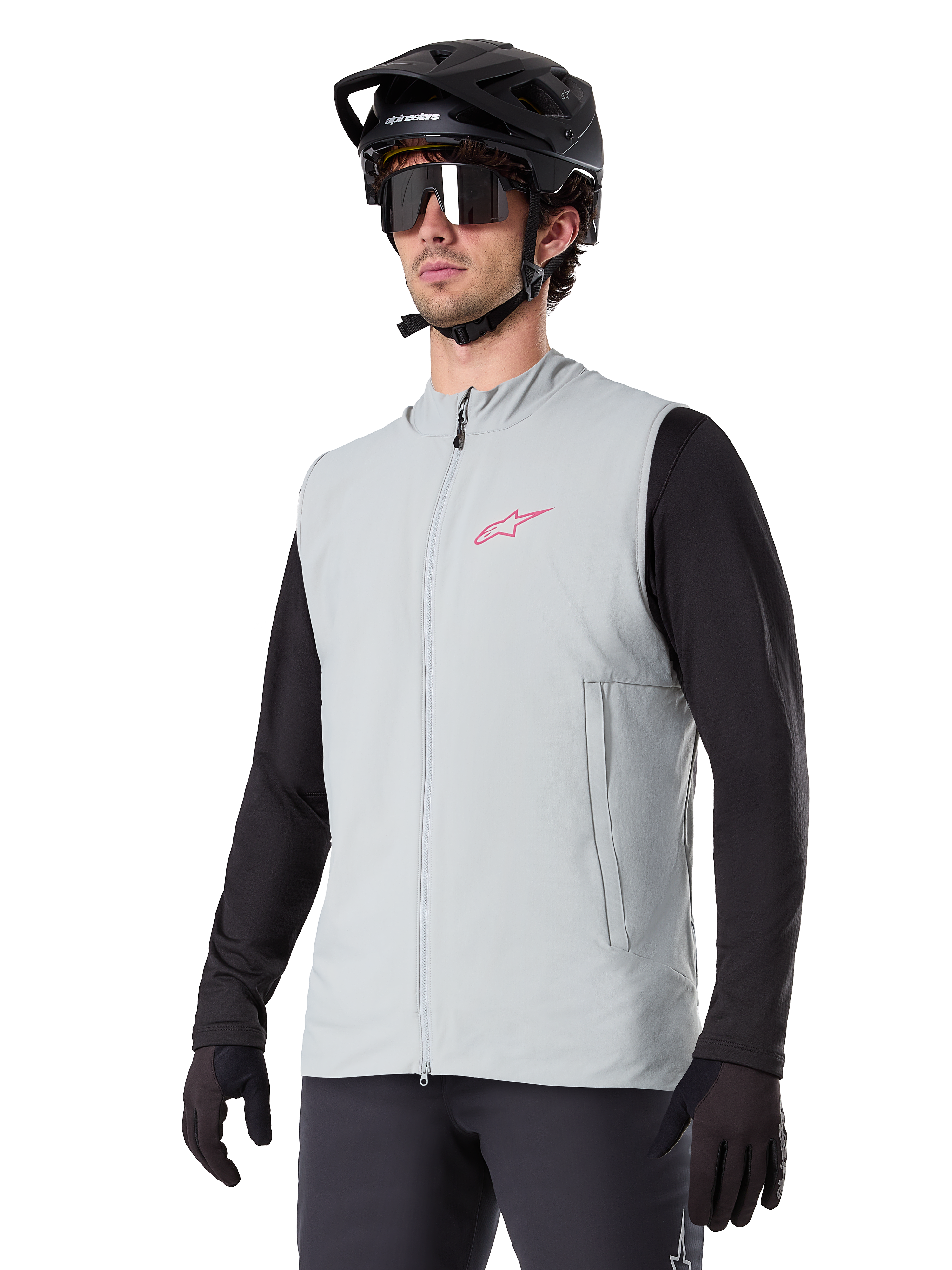 Alpinestars A-Dura Thermal Vest, titaniumgrå, isoleret cykelvest, båret over en sort langærmet trøje med sort mountainbikehjelm og handsker, med pink logo på brystet og lodrette sidelommer med lynlås