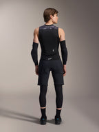 Alpinestars A-Motion Plasma beskyttelsesvest, set bagfra, sort med grå camo-detaljer på skuldrene, båret af model med sorte albuebeskyttere, cykelshorts over leggings og sorte cykelsko, der viser den integrerede rygbeskytter