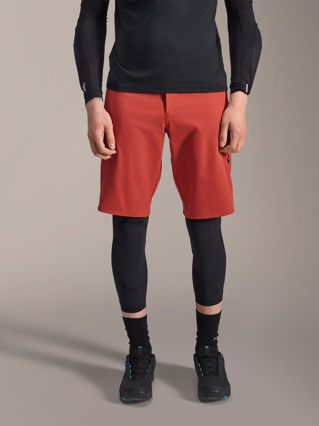 Alpinestars A-Motion Plasma knæbeskytter, sort MTB-knæbeskytter, båret med røde shorts og sort langærmet top, ergonomisk design med slank profil, letvægts mesh-konstruktion til off-road kørsel