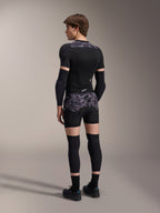 Model iført Alpinestars A-Motion Plasma Protection Boxers i Black Camo og matchende A-Motion Plasma Protection Jacket, set bagfra med gråt camouflage-mønster, albuebeskyttere, knæbeskyttere og cykelsko, komplet beskyttelsesudstyr til mountainbike.