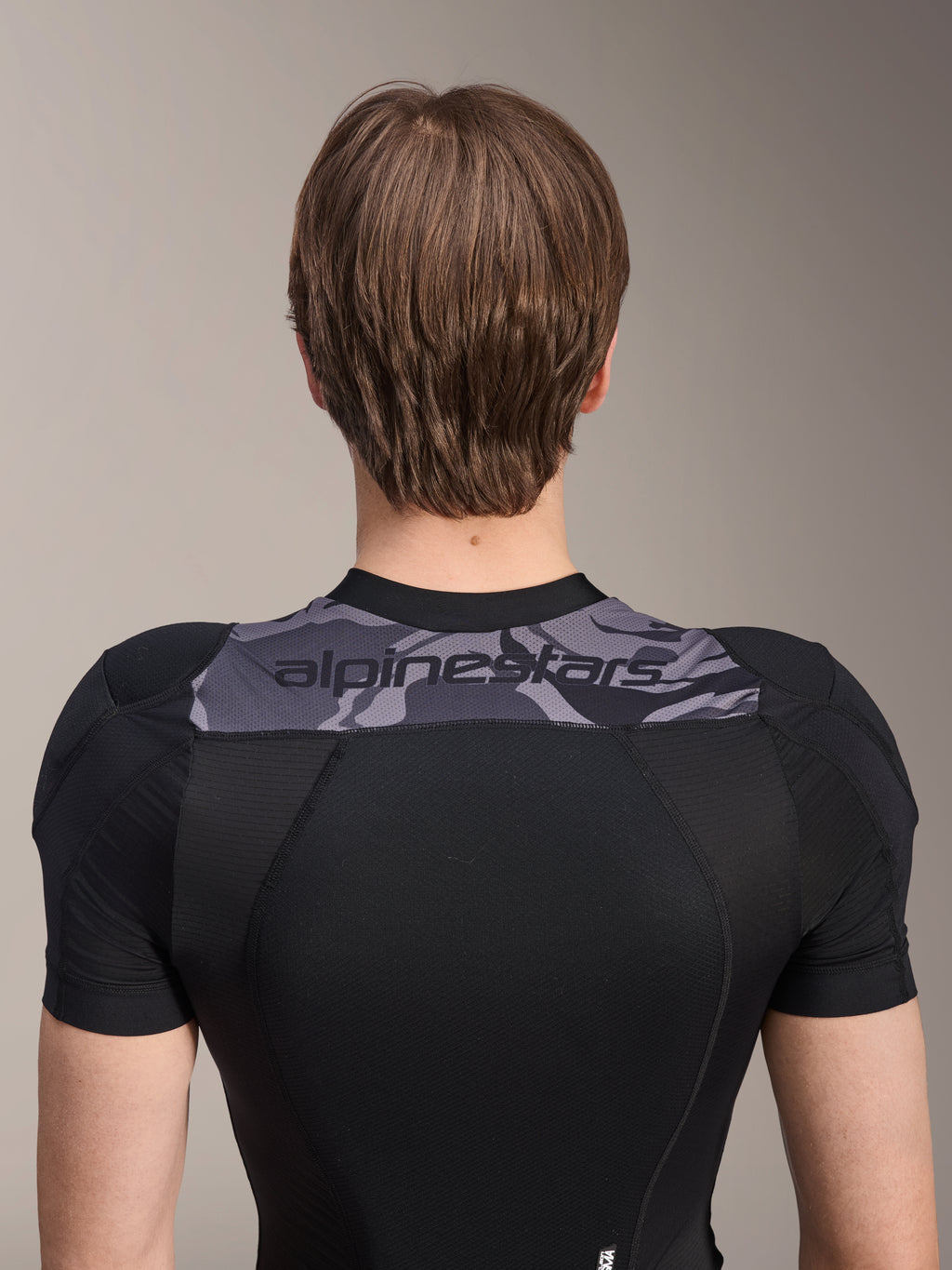 Alpinestars A-Motion Plasma beskyttelsesjakke - kortærmet, set bagfra af den øvre torso, sort med gråt camo-panel over skuldrene med Alpinestars-logo, åndbar strækbar mesh-konstruktion til MTB-beskyttelse