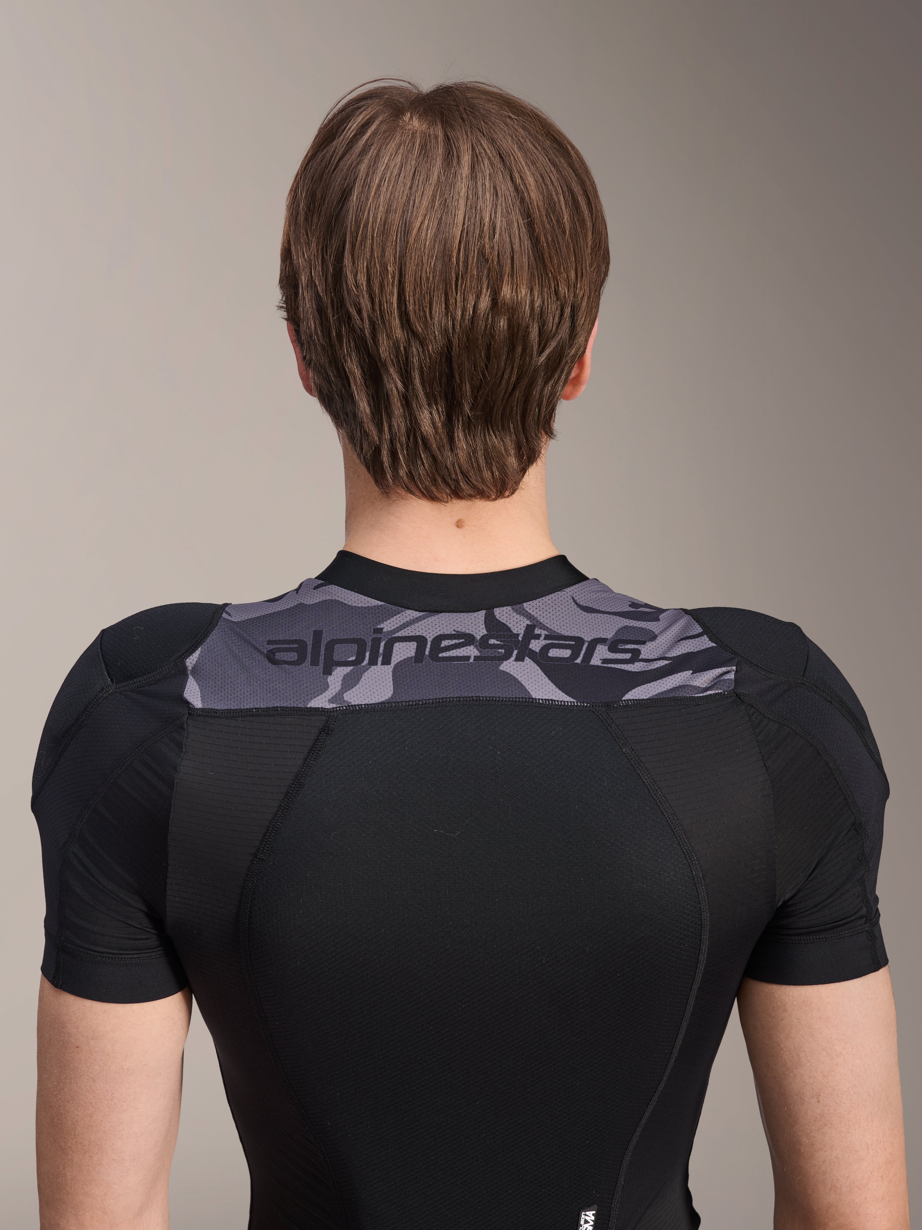 Alpinestars A-Motion Plasma beskyttelsesjakke - kortærmet, set bagfra af den øvre torso, sort med gråt camo-panel over skuldrene med Alpinestars-logo, åndbar strækbar mesh-konstruktion til MTB-beskyttelse