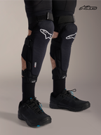 Alpinestars A-Impact Plasma Pro Knee Shin Protectors, mountain bike knee guards in black with white logo, worn by a model showcasing triple strap closure and Nucleon Plasma protection