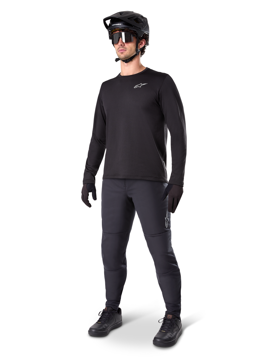 Mountainbike-rytter iført Alpinestars A-Dura termobukser, sorte, stylet med en sort langærmet trøje, sort hjelm og solbriller, med et sølvfarvet Alpinestars-logo på venstre lår, designet til MTB-kørsel i koldt vejr