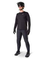 Mountainbike-rytter iført Alpinestars A-Dura termobukser, sorte, stylet med en sort langærmet trøje, sort hjelm og solbriller, med et sølvfarvet Alpinestars-logo på venstre lår, designet til MTB-kørsel i koldt vejr