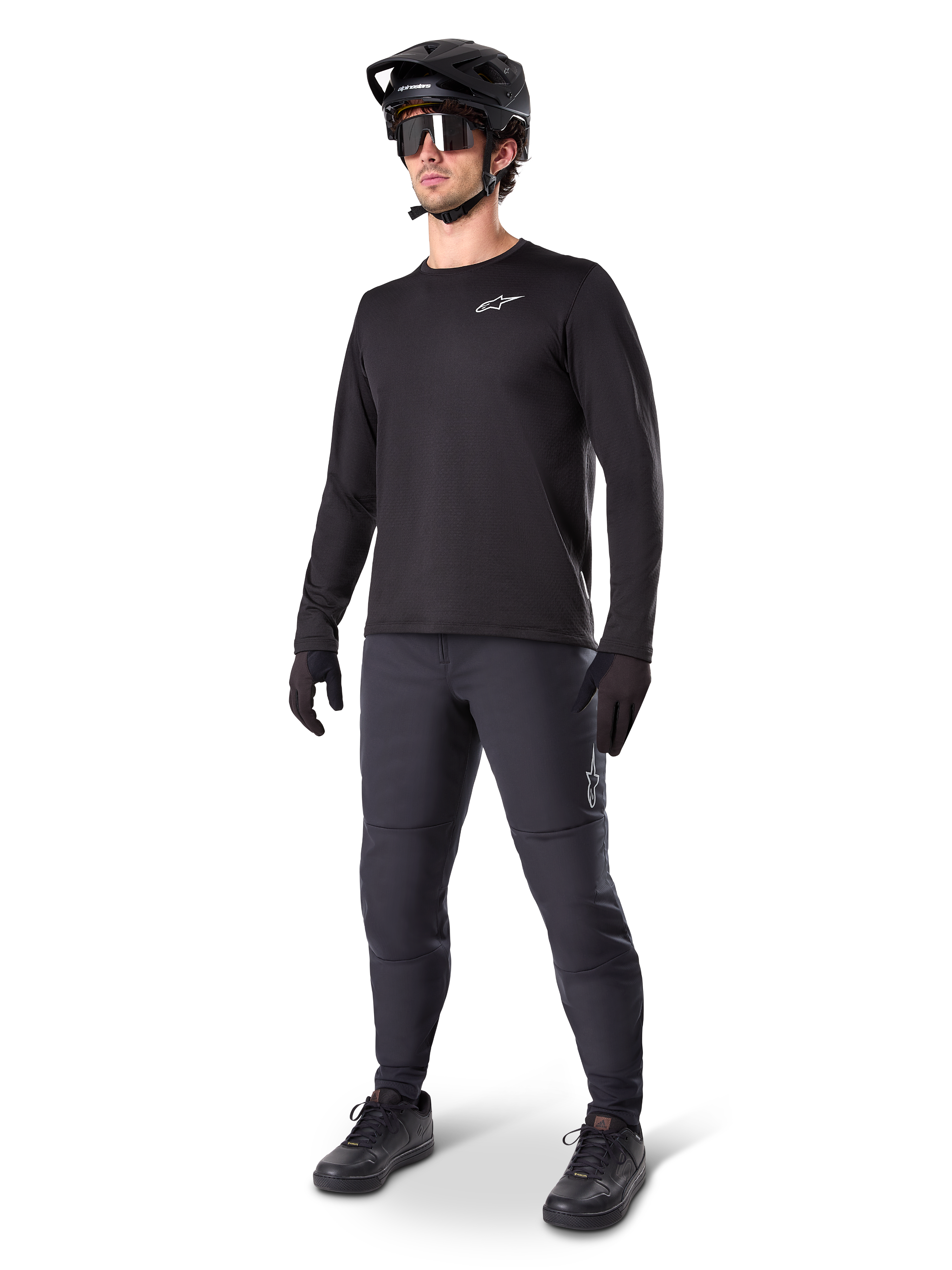 Mountainbike-rytter iført Alpinestars A-Dura termobukser, sorte, stylet med en sort langærmet trøje, sort hjelm og solbriller, med et sølvfarvet Alpinestars-logo på venstre lår, designet til MTB-kørsel i koldt vejr