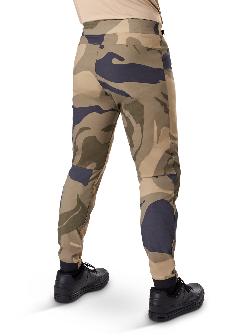 Alpinestars A-Dura Camo bukser, MTB-bukser, brunt camouflagemønster med sandfarvede og mørkegrå detaljer, set bagfra med sorte sneakers, med tapered ben og elastiske manchetter, slidstærkt 2-vejs strækstof til mountainbike