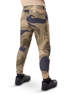 Alpinestars A-Dura Camo bukser, MTB-bukser, brunt camouflagemønster med sandfarvede og mørkegrå detaljer, set bagfra med sorte sneakers, med tapered ben og elastiske manchetter, slidstærkt 2-vejs strækstof til mountainbike