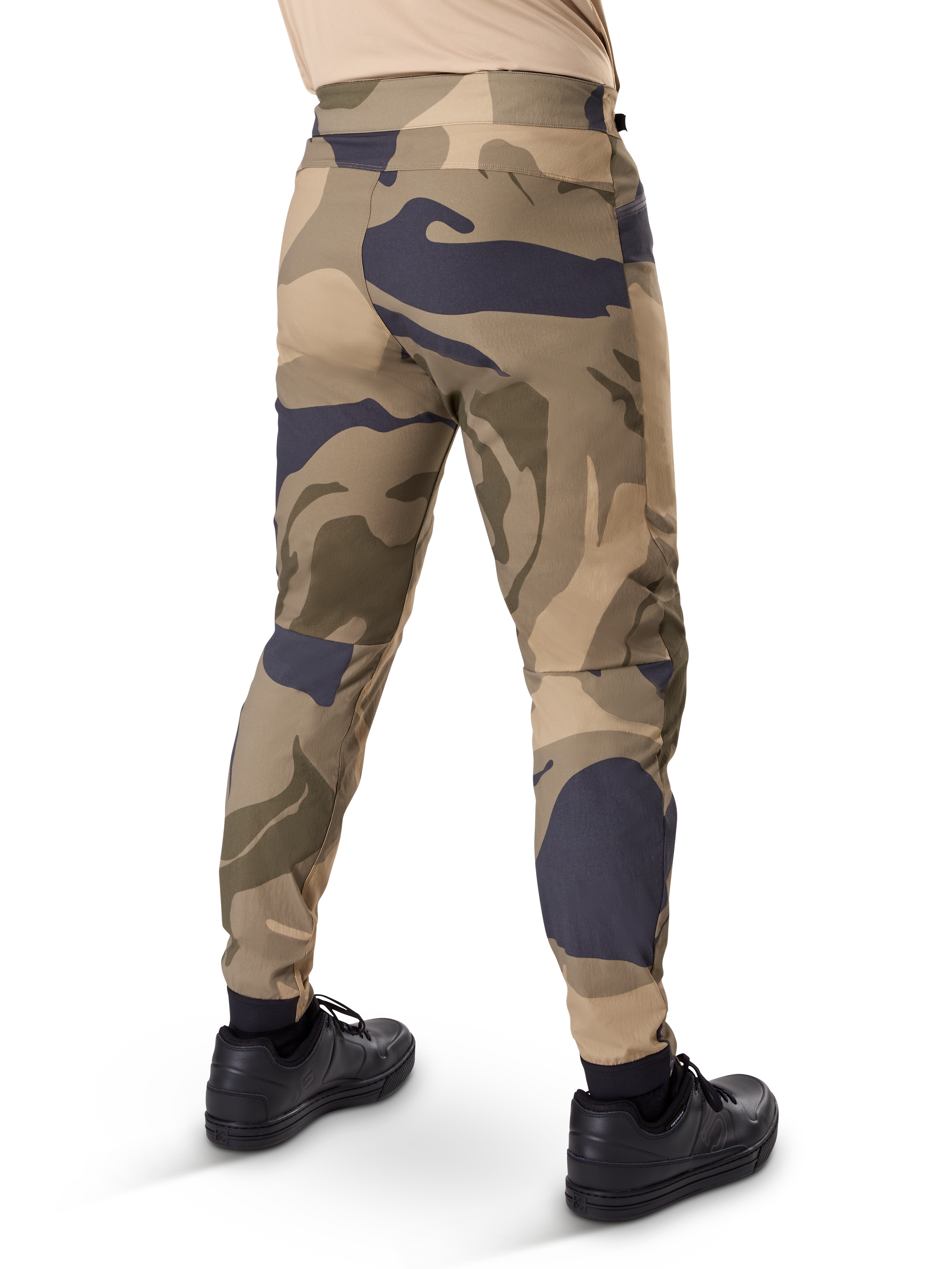 Alpinestars A-Dura Camo bukser, MTB-bukser, brunt camouflagemønster med sandfarvede og mørkegrå detaljer, set bagfra med sorte sneakers, med tapered ben og elastiske manchetter, slidstærkt 2-vejs strækstof til mountainbike