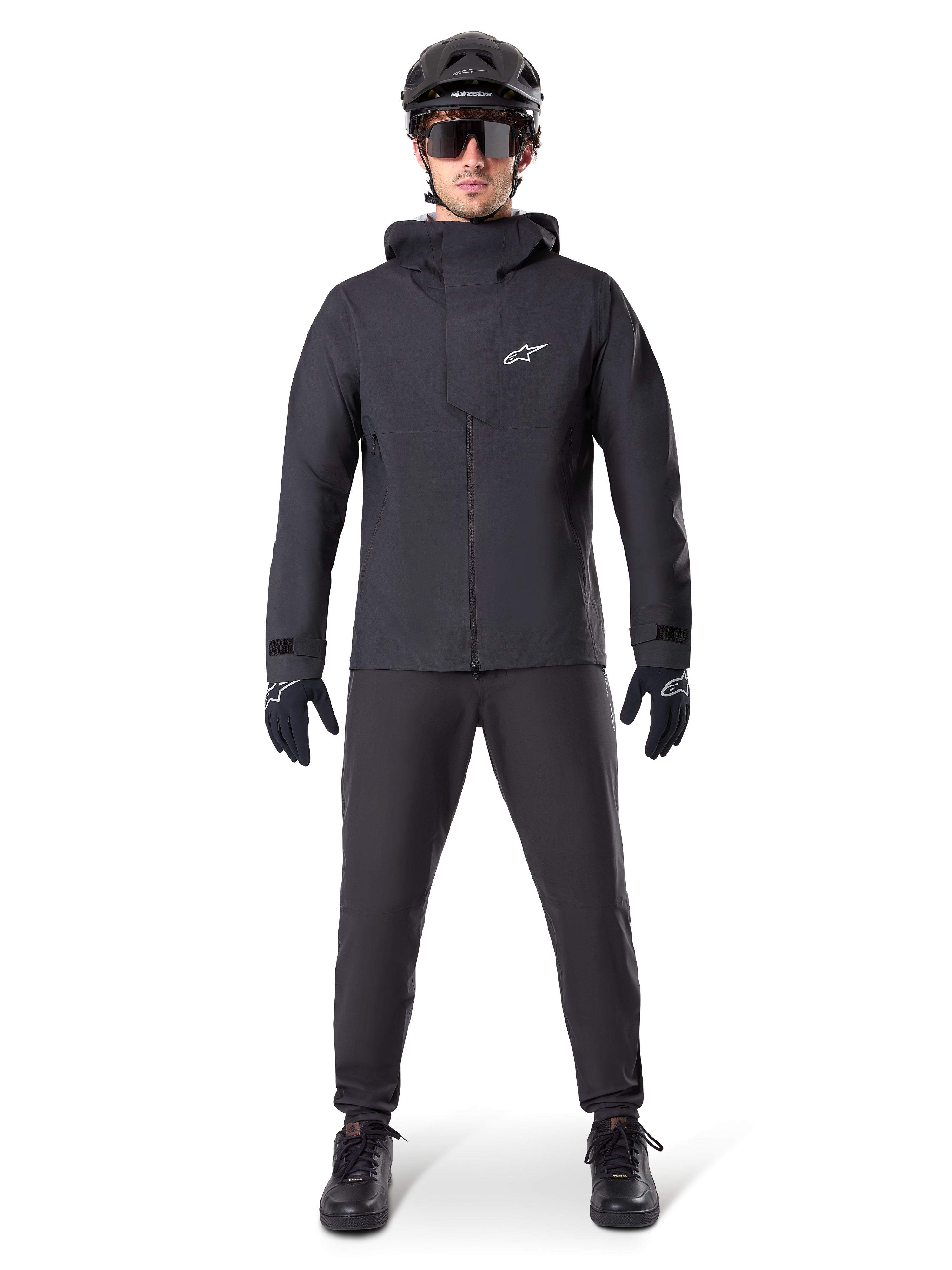 Alpinestars A-Dura Waterproof Pants, sorte MTB-bukser, båret som en del af et komplet helt sort mountainbike-udstyrssæt inklusiv en teknisk vandtæt jakke, sort hjelm, solbriller og handsker, designet til terrænkørsel i vådt vejr.