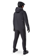Alpinestars A-Dura Waterproof Pants, MTB-bukser, sort, set bagfra på en rytter iført et komplet sort mountainbike-outfit inklusive en jakke med hætte og hjelm, slidstærkt vandtæt udstyr til mudrede stier