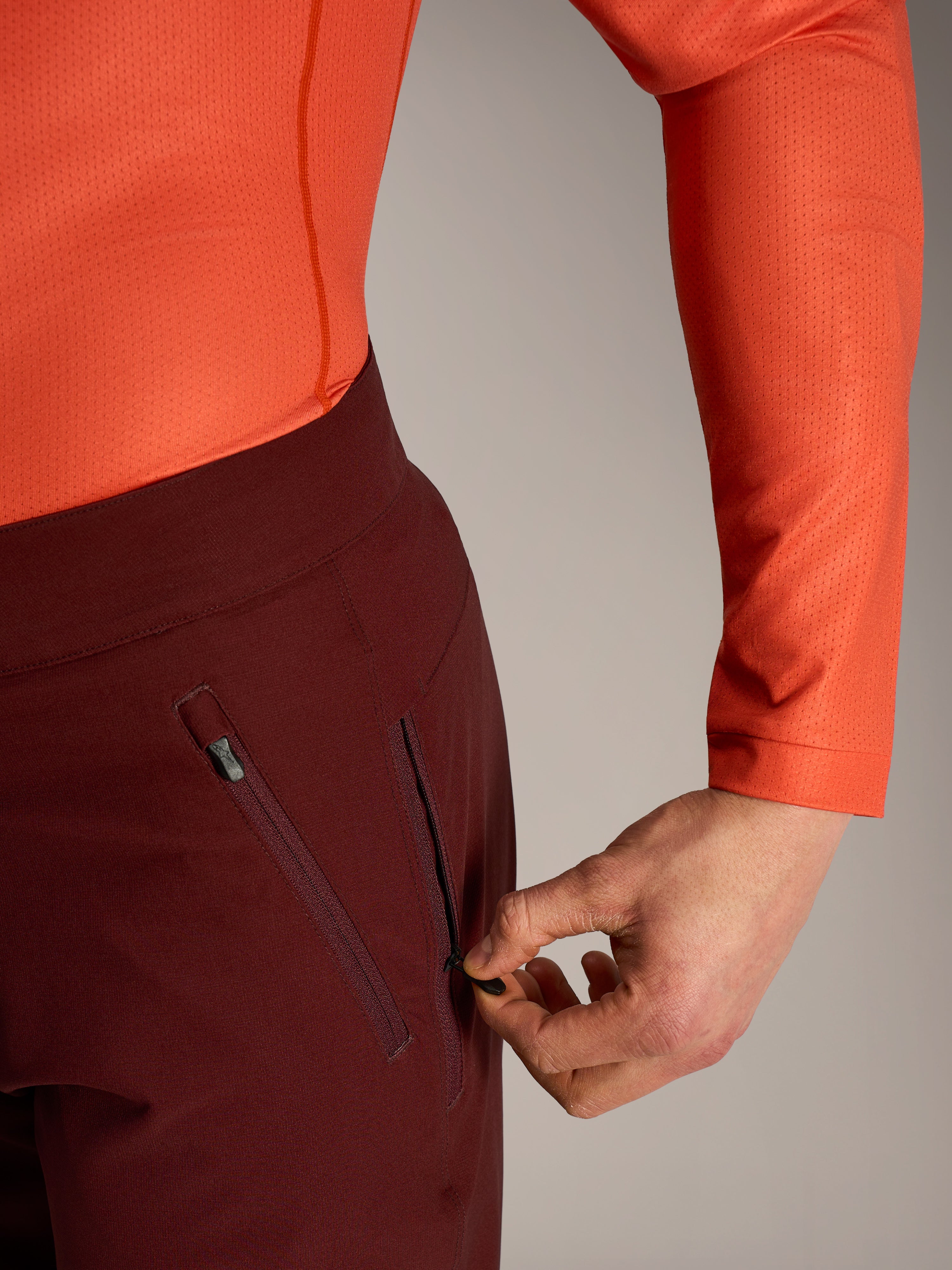 Alpinestars A-Dura Ride shorts i bordeaux, detalje af hånd der åbner en sikker sidelomme med lynlås og mesh-for.