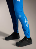 A-Supra Elite Bukser i Faded Bright Blue med hvidt Astars-logo på underbenet og sorte MTB-sko.