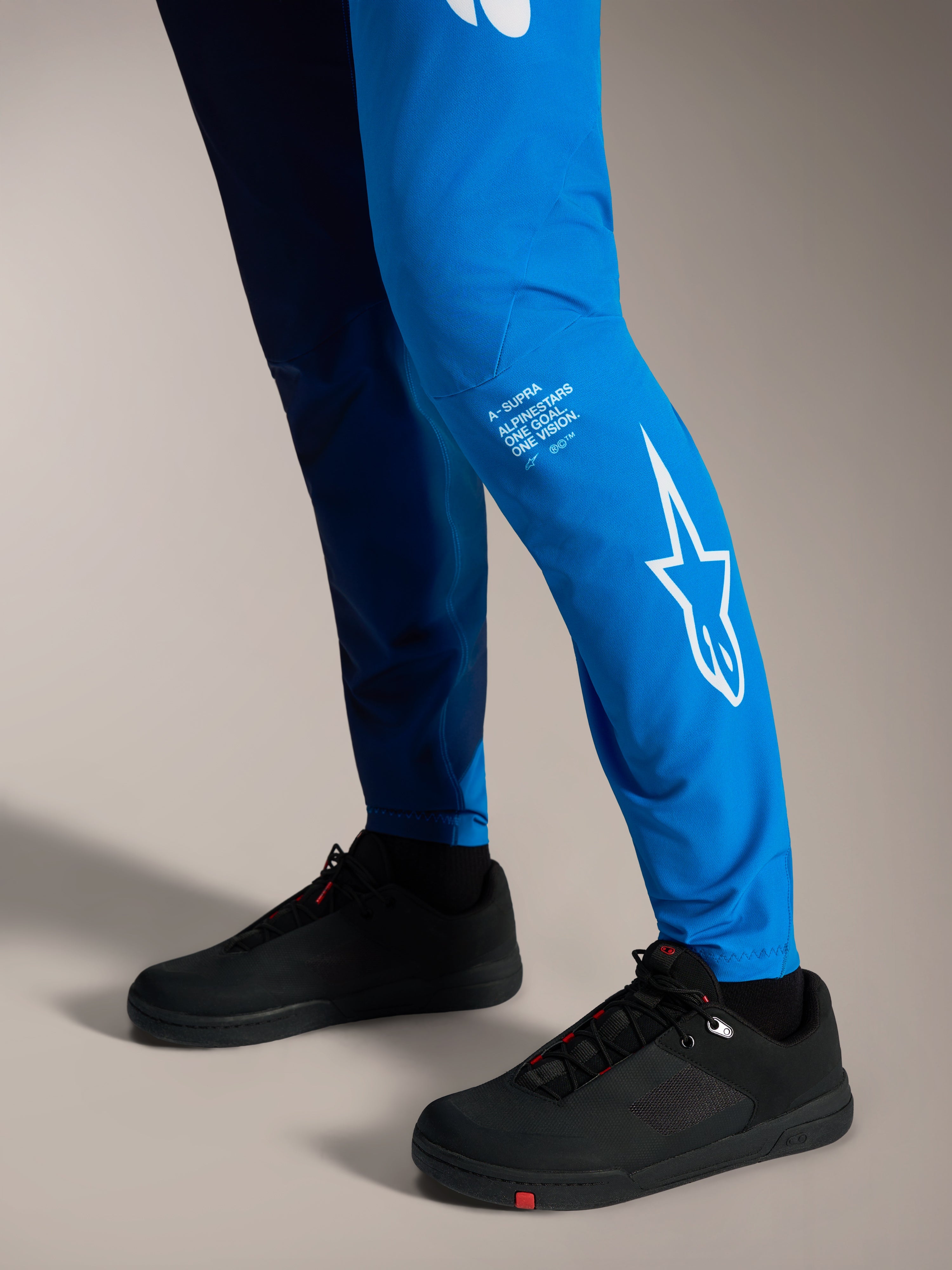 A-Supra Elite Bukser i Faded Bright Blue med hvidt Astars-logo på underbenet og sorte MTB-sko.