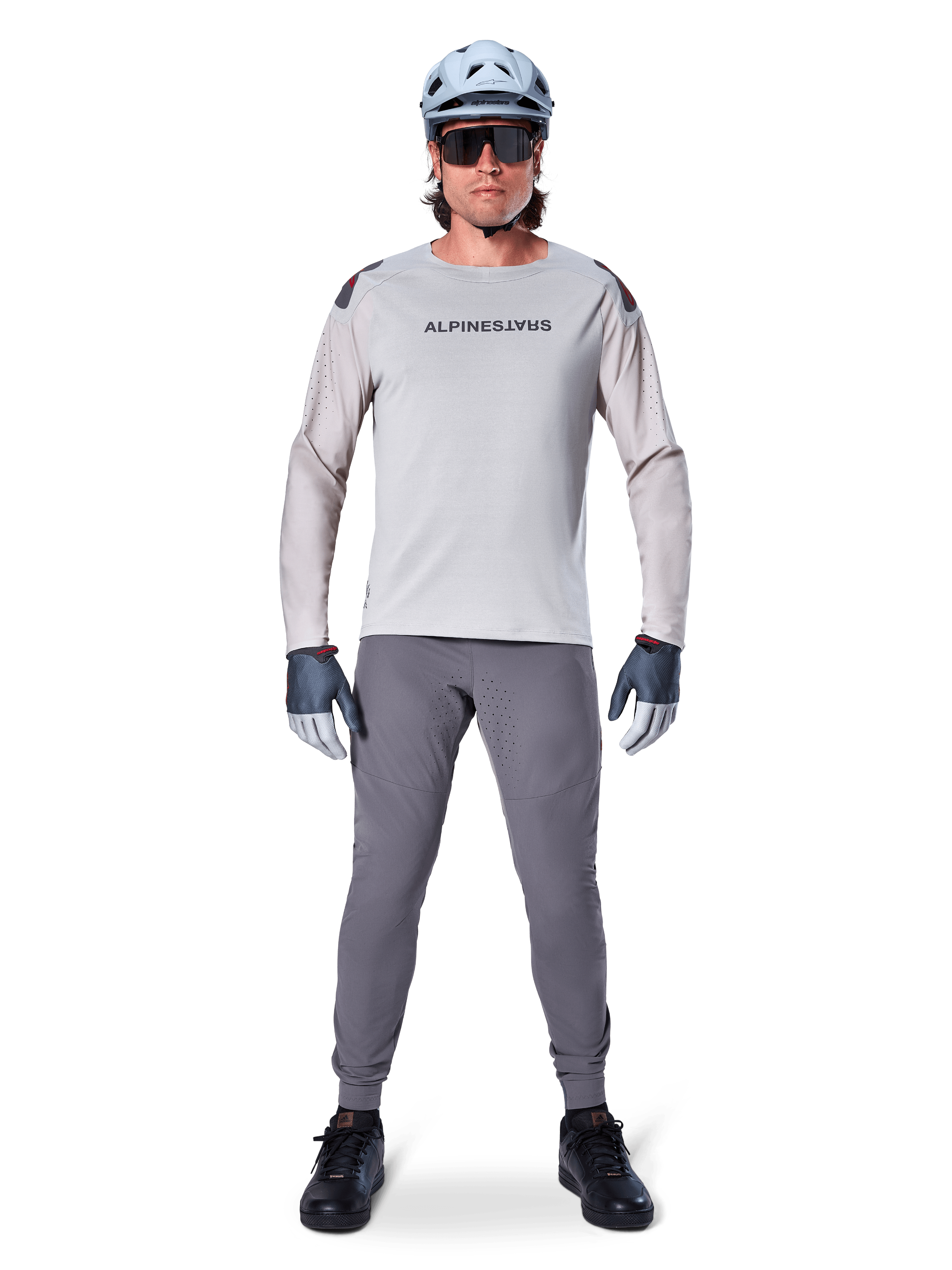 Alpinestars A-Aria Elite bukser, mørkegrå mountainbike-bukser, båret af en rytter i en lysegrå langærmet trøje, lyseblå hjelm og sorte sko, med synlige laserperforeringer på indersiden af benene og en tætsiddende ydelsespasform.