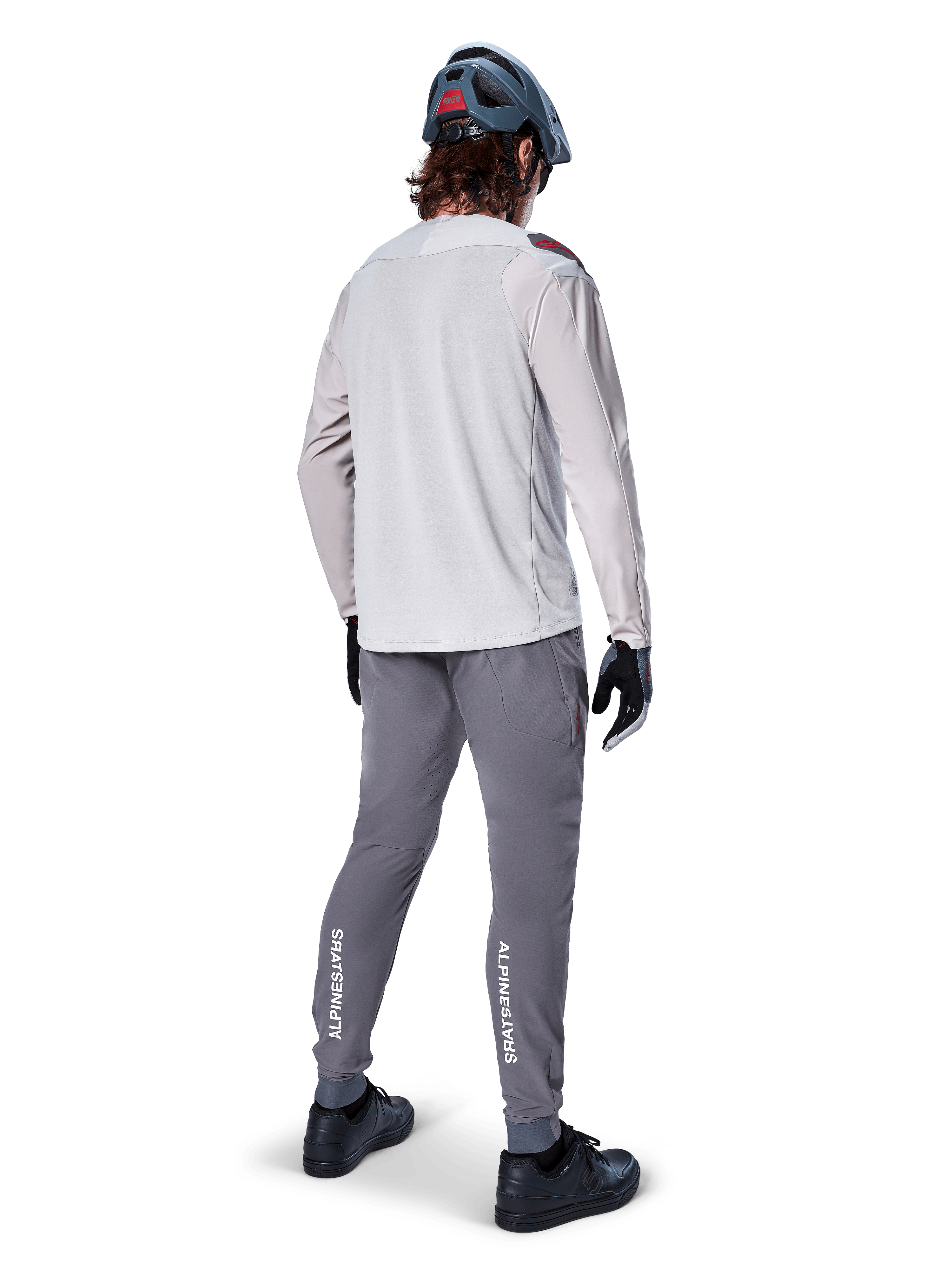 Alpinestars A-Aria Elite bukser, MTB cykelbukser, mørkegrå, set bagfra af en rytter iført et komplet outfit, med hvid Alpinestars-branding på underbenene, performance-pasform med laserperforeringer, kombineret med en lysegrå langærmet trøje og grå MTB-hjelm
