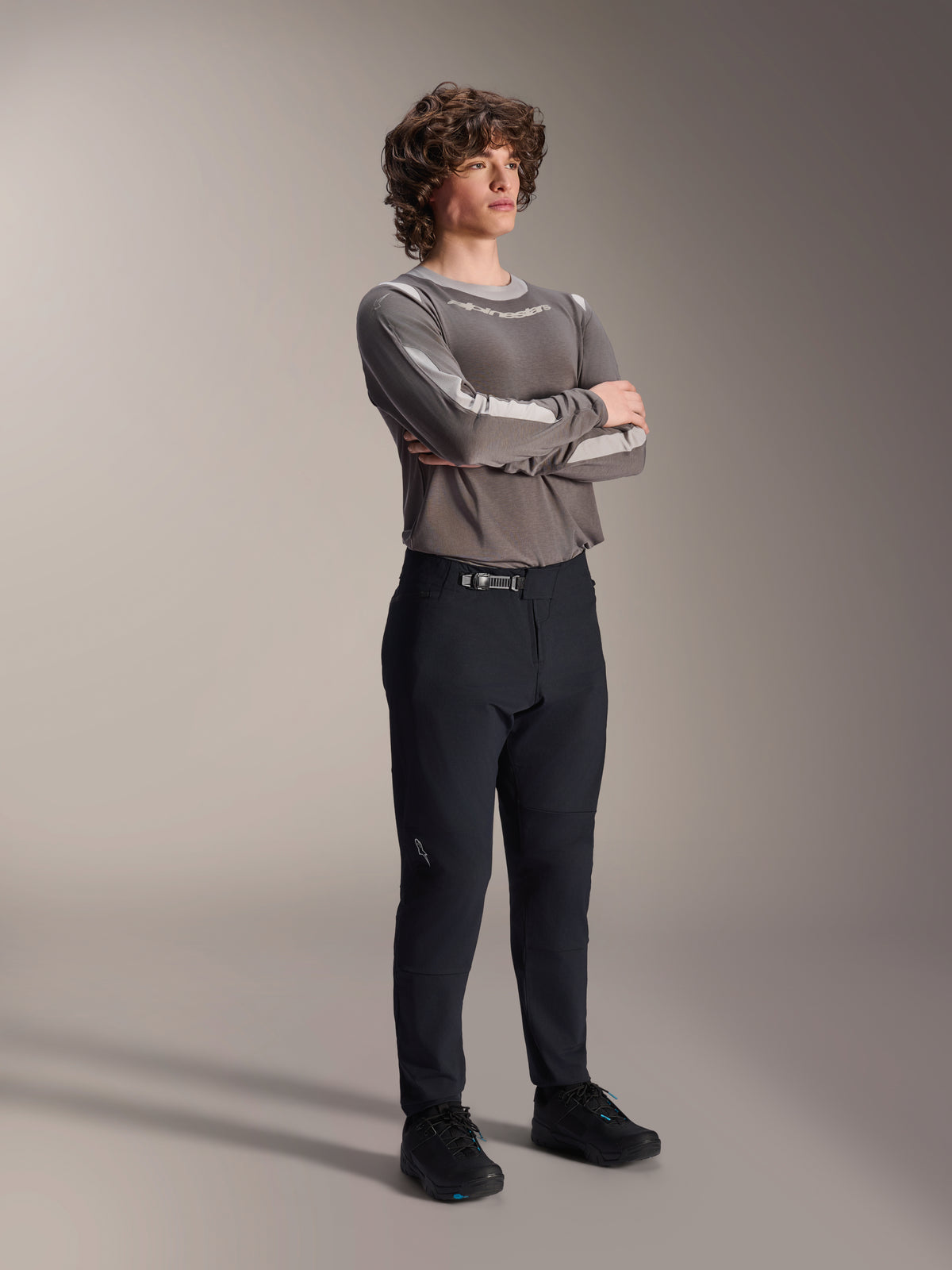 Mandlig model iført Alpinestars A-Dura Elite bukser, sorte MTB-bukser, kombineret med en grå langærmet jersey og sorte cykelsko, front rachet-lukkesystem, professionelt mountainbike-tøj til trail- og endurokørsel