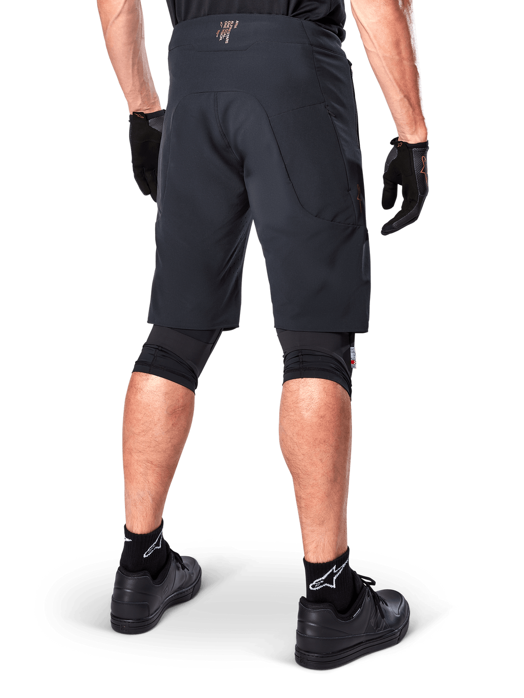 Bagfra af en rytter iført Alpinestars A-Aria Elite Shorts i sort, performance mountainbike-shorts, kombineret med sorte cykelhandsker og sorte sko, designet til fleksibel bevægelse på off-road stier