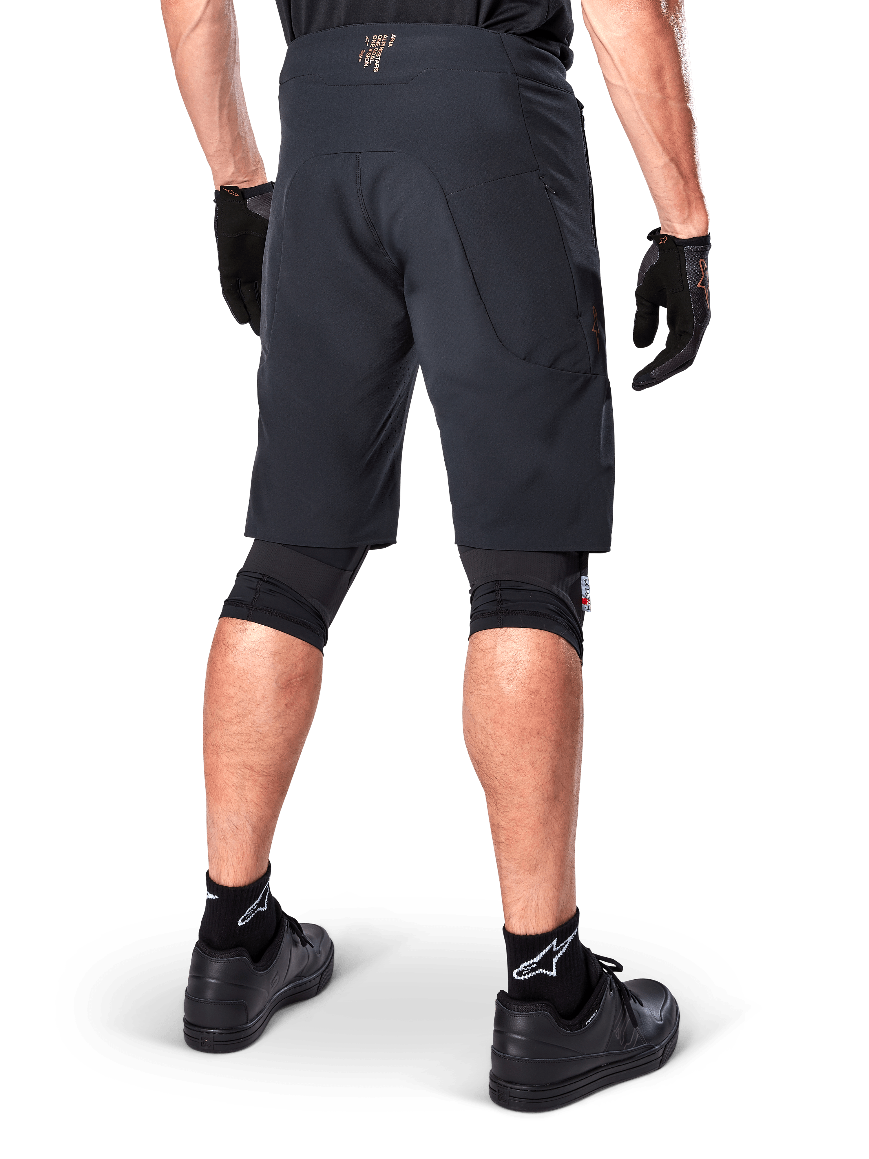 Bagfra af en rytter iført Alpinestars A-Aria Elite Shorts i sort, performance mountainbike-shorts, kombineret med sorte cykelhandsker og sorte sko, designet til fleksibel bevægelse på off-road stier