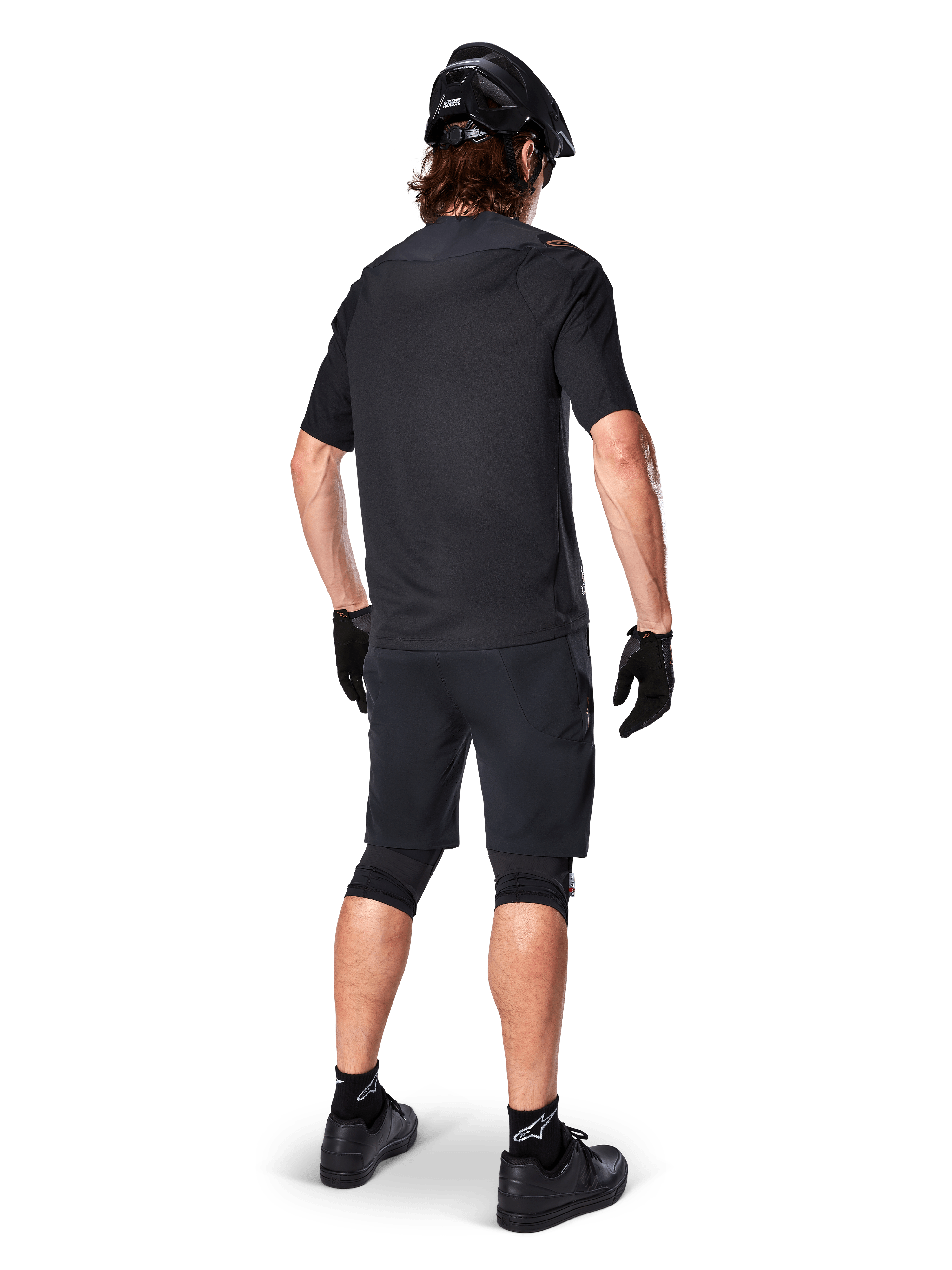 Set bagfra af en mountainbiker iført Alpinestars A-Aria Elite Shorts i sort, kombineret med en matchende sort kortærmet jersey, sort hjelm, handsker og MTB-sko, der viser et komplet performance-outfit til off-road cykling.
