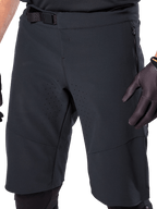 Alpinestars A-Aria Elite Shorts i sort, nærbillede af talje- og lårområdet, med magnetisk spændelukning, lynlåslommer og laserskårne ventilationsperforeringer, båret med sorte cykelhandsker til mountainbike.