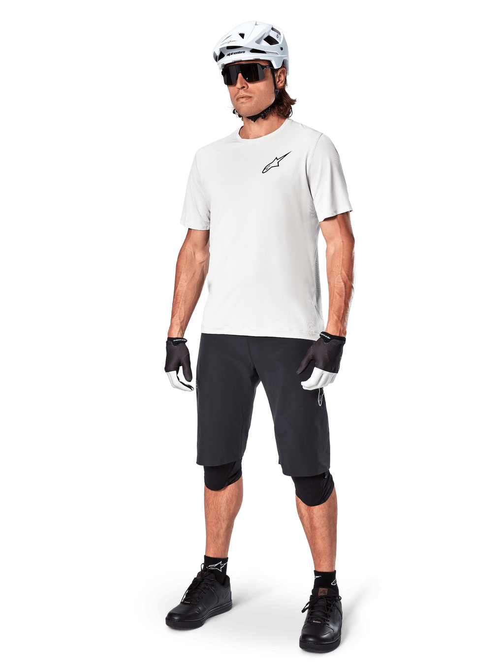 Mandlig mountainbiker iført Alpinestars A-Aria shorts, sorte cykelshorts, stylat med en hvid kortærmet trøje, hvid mountainbikehjelm og sort performance-udstyr, komplet outfit til off-road trailkørsel