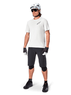 Mandlig mountainbiker iført Alpinestars A-Aria shorts, sorte cykelshorts, stylat med en hvid kortærmet trøje, hvid mountainbikehjelm og sort performance-udstyr, komplet outfit til off-road trailkørsel