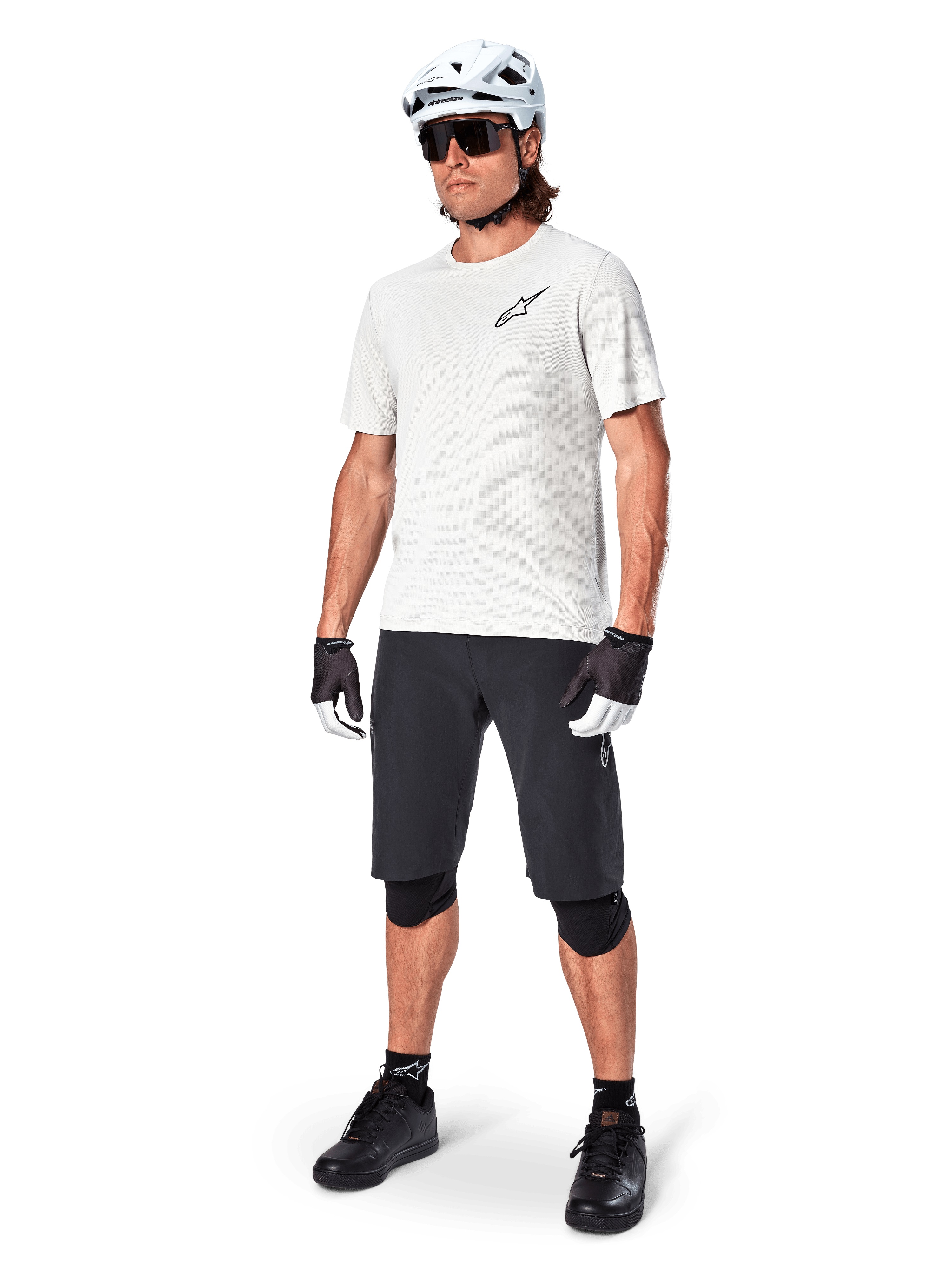 Mandlig mountainbiker iført Alpinestars A-Aria shorts, sorte cykelshorts, stylat med en hvid kortærmet trøje, hvid mountainbikehjelm og sort performance-udstyr, komplet outfit til off-road trailkørsel
