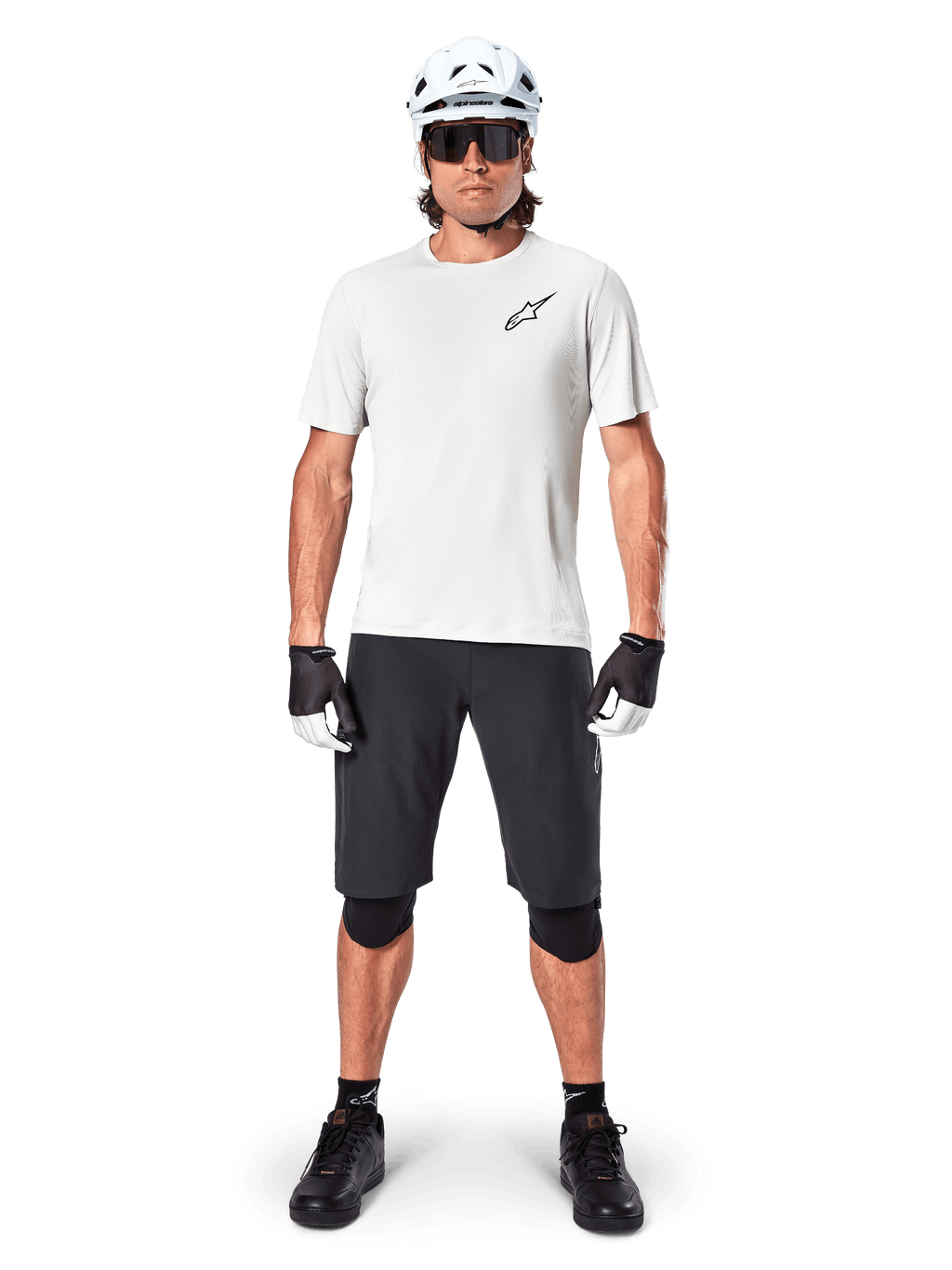 Mandlig mountainbiker iført Alpinestars A-Aria Shorts, sort, kombineret med en hvid performance-trøje, hvid hjelm og sorte knæbeskyttere, professionelt off-road cykeludstyr set forfra i fuld figur