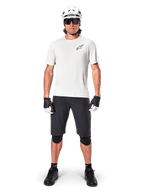Mandlig mountainbiker iført Alpinestars A-Aria Shorts, sort, kombineret med en hvid performance-trøje, hvid hjelm og sorte knæbeskyttere, professionelt off-road cykeludstyr set forfra i fuld figur