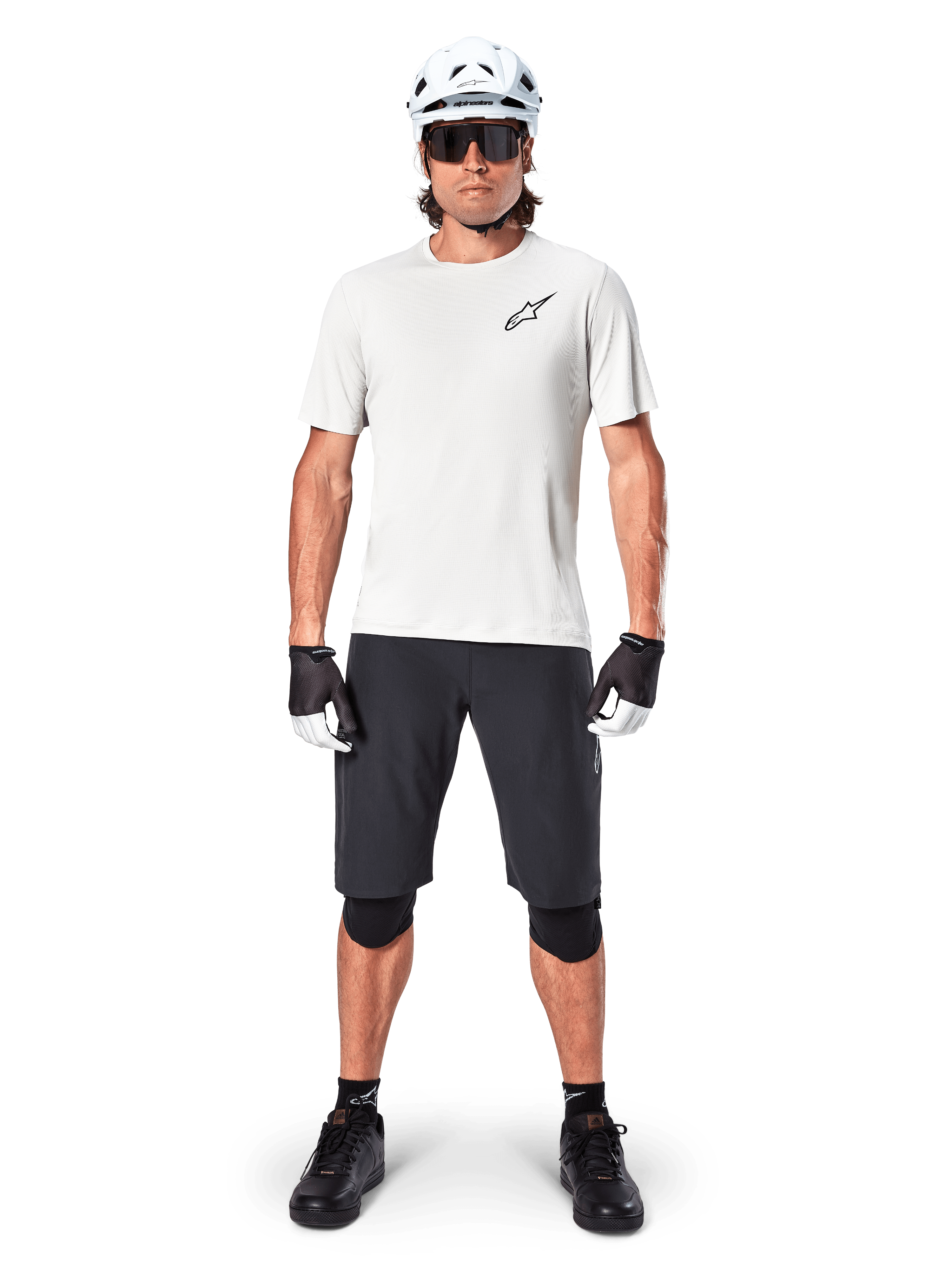 Mandlig mountainbiker iført Alpinestars A-Aria Shorts, sort, kombineret med en hvid performance-trøje, hvid hjelm og sorte knæbeskyttere, professionelt off-road cykeludstyr set forfra i fuld figur