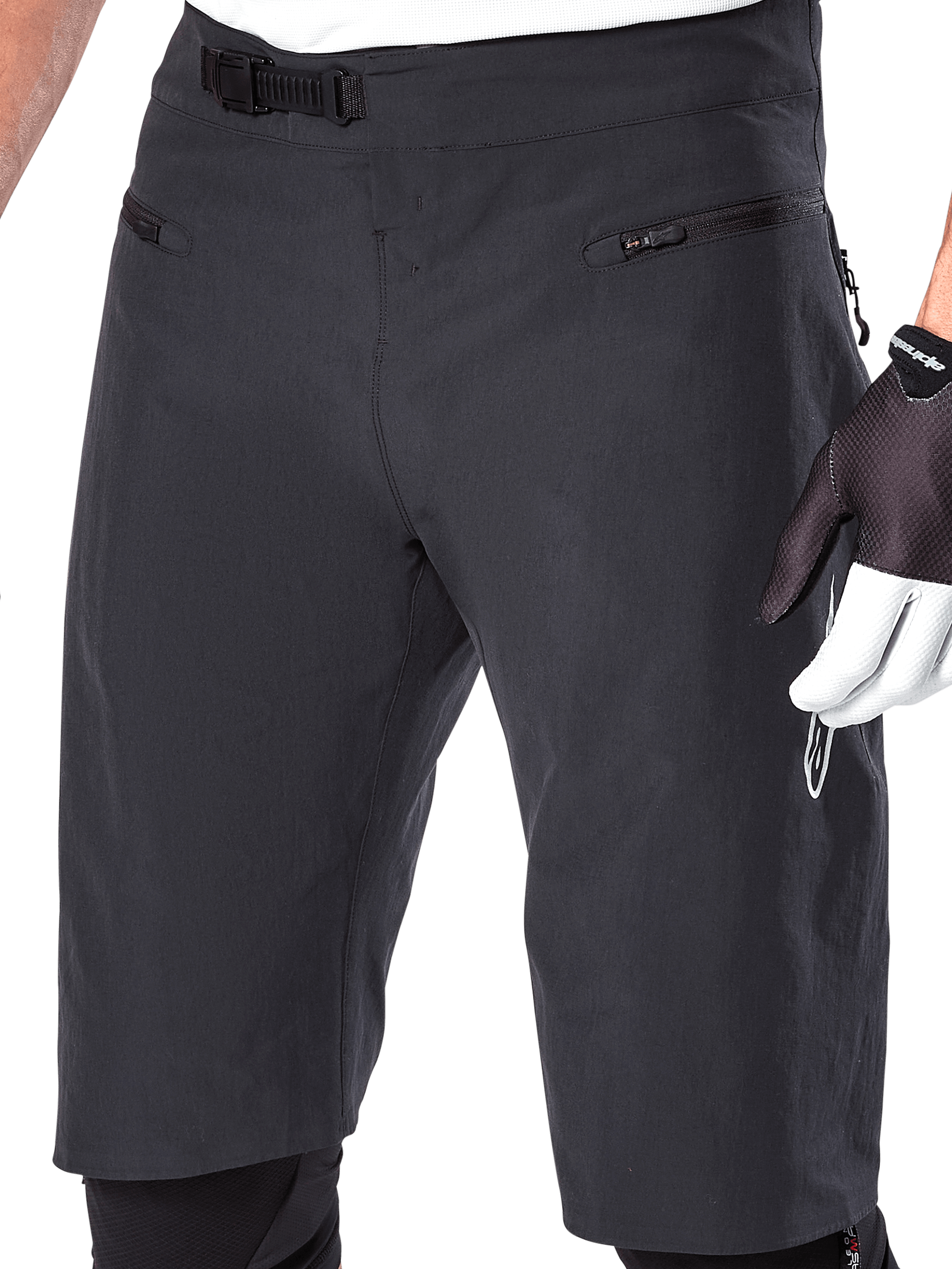 Alpinestars A-Aria Shorts, mountainbike-shorts, sort, nærbillede af taljen og lårene foran, der viser ratchet-lukkesystemet og lynlåslommer, bæres med sort-hvide cykelhandsker, performance trail-udstyr.
