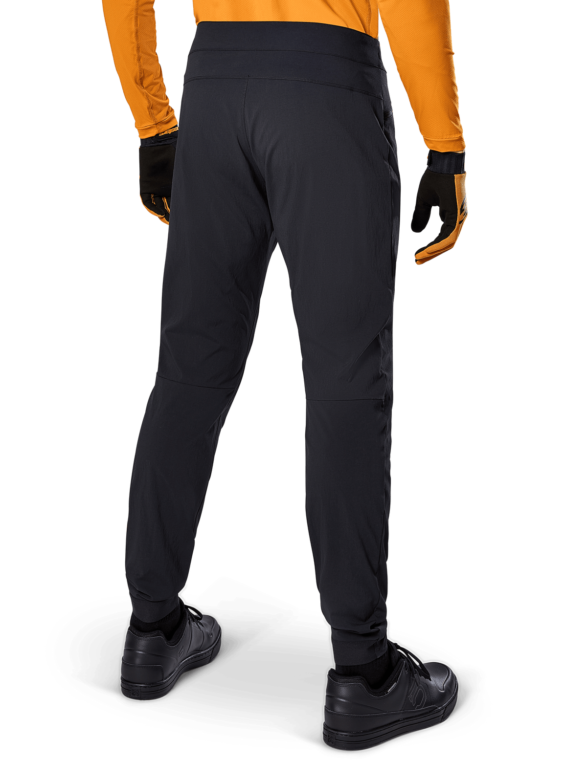 Alpinestars A-Dura bukser, sorte MTB-bukser, set bagfra, båret med en orange langærmet trøje og sorte handsker, med elastiske manchetter og slidstærkt tekstilmateriale til mountainbiking
