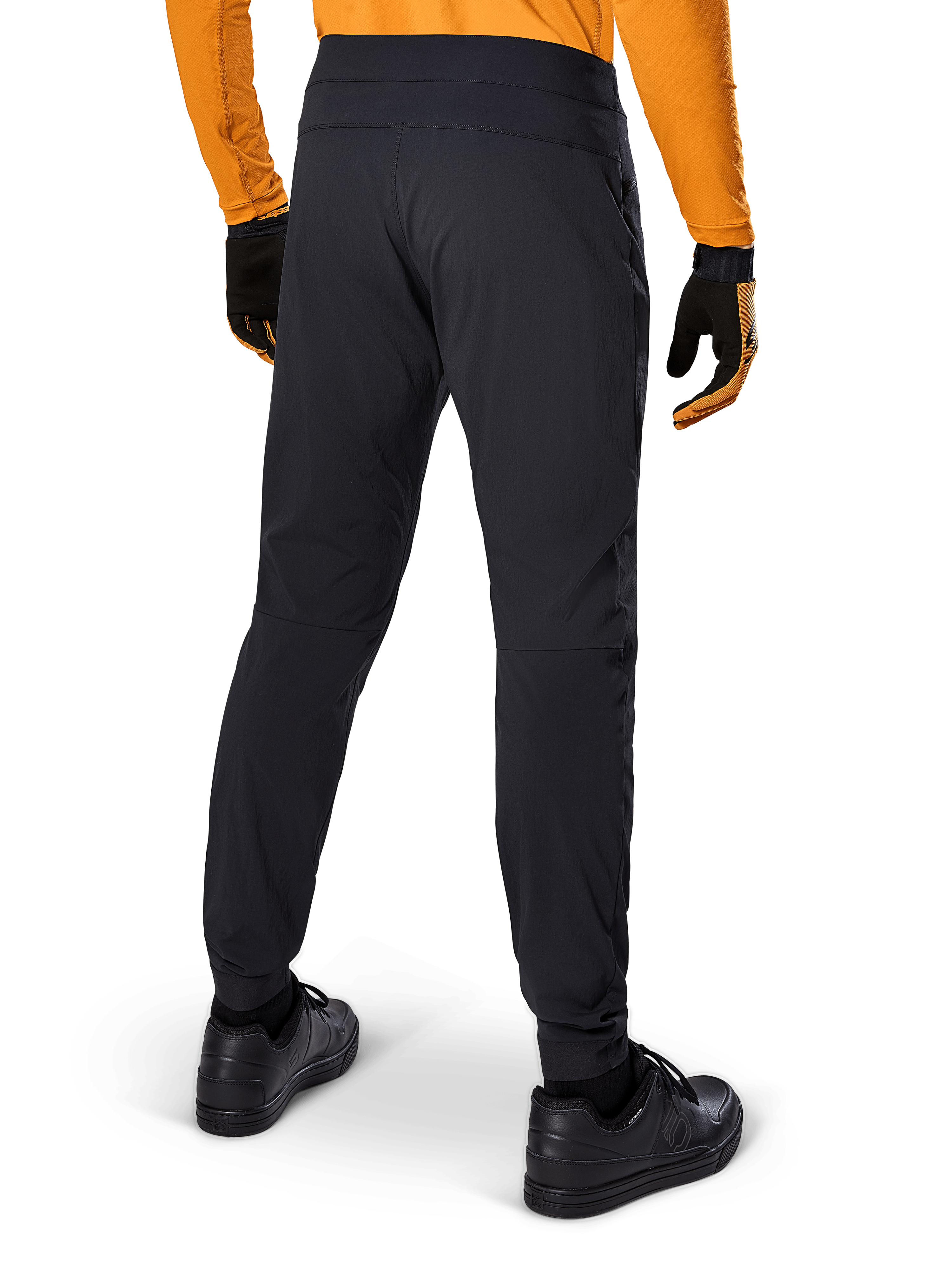Alpinestars A-Dura bukser, sorte MTB-bukser, set bagfra, båret med en orange langærmet trøje og sorte handsker, med elastiske manchetter og slidstærkt tekstilmateriale til mountainbiking
