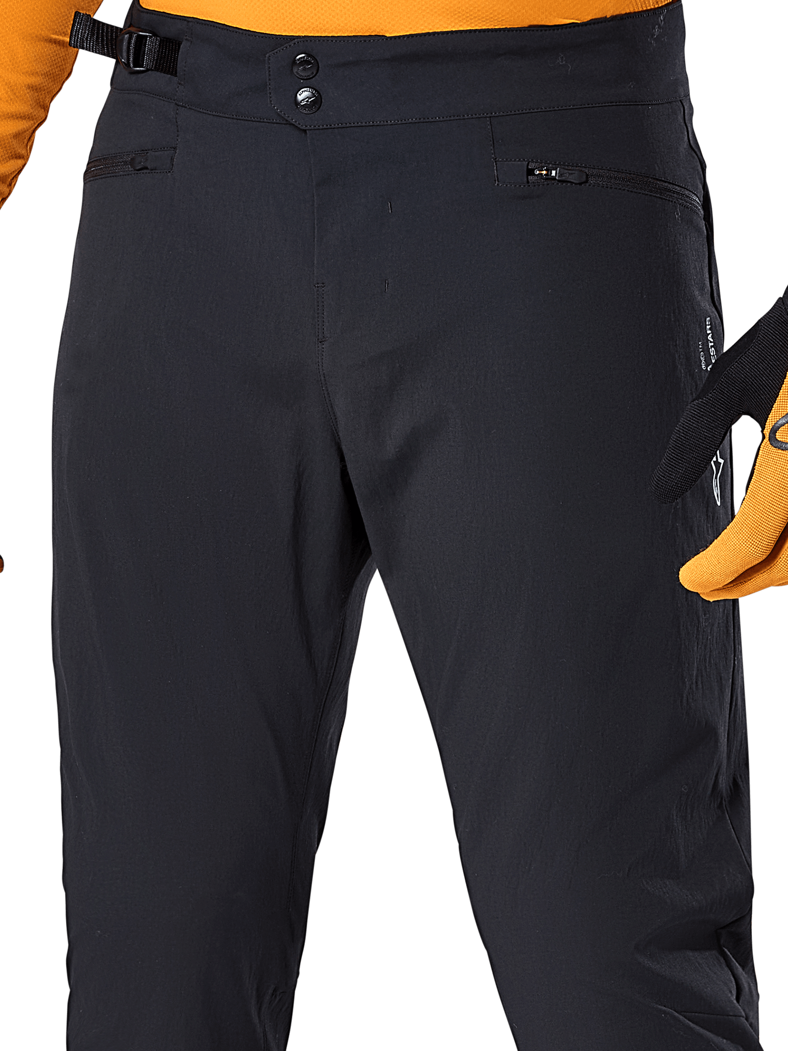 Alpinestars A-Dura bukser, sorte MTB-cykelbukser, nærbillede med dobbelt trykknaplukning i taljen, justerbar sideklemme og lynlåslommer, kombineret med en orange trøje og handsker
