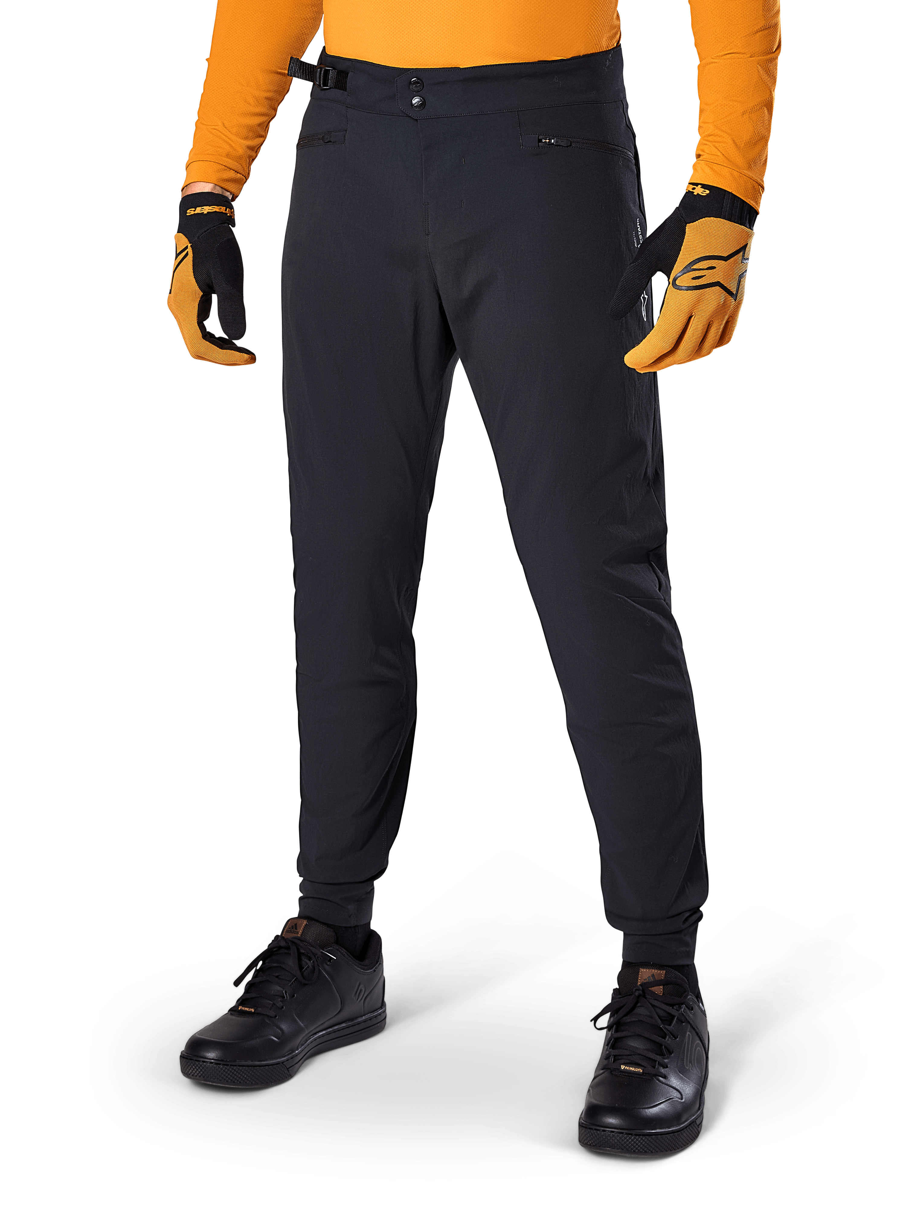Alpinestars A-Dura bukser, mountainbike-bukser, sorte, sidejustering i taljen og lynlåslommer, båret med orange trøje og handsker, sporty regulær pasform til MTB-kørsel