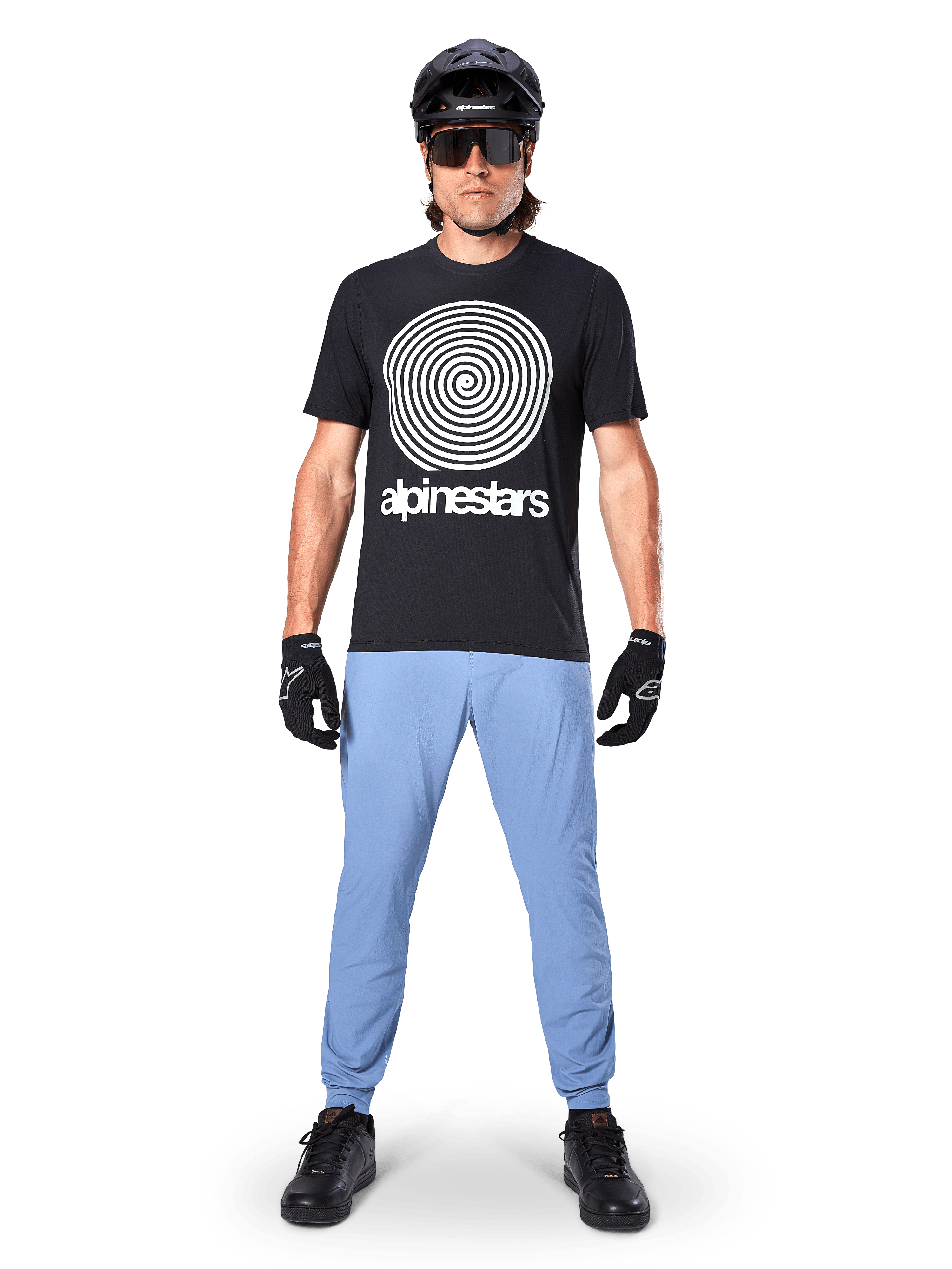 Alpinestars A-Dura bukser, Infinity Blue, MTB-bukser båret med en sort t-shirt med spiralgrafik, sorte handsker og en sort hjelm, med slidstærkt strækstof og elastiske manchetter, performance mountainbike-udstyr