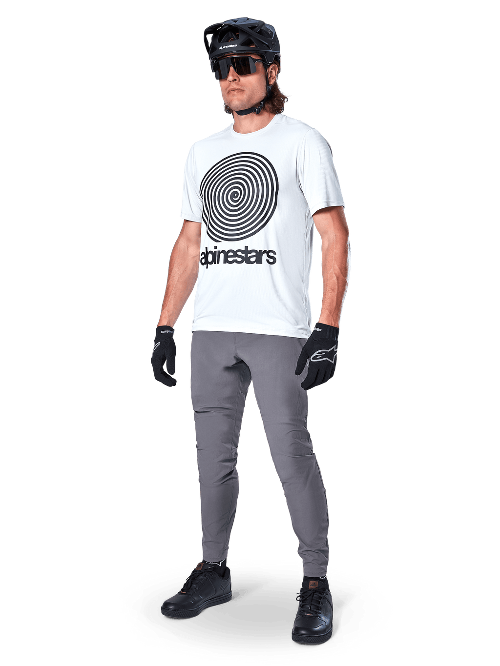 Alpinestars A-Dura bukser, MTB-bukser, mørkegrå, båret med hvid t-shirt med spiralgrafik, sort MTB-hjelm, solbriller og sorte handsker, holdbart 2-vejs strækstof til terrænkørsel