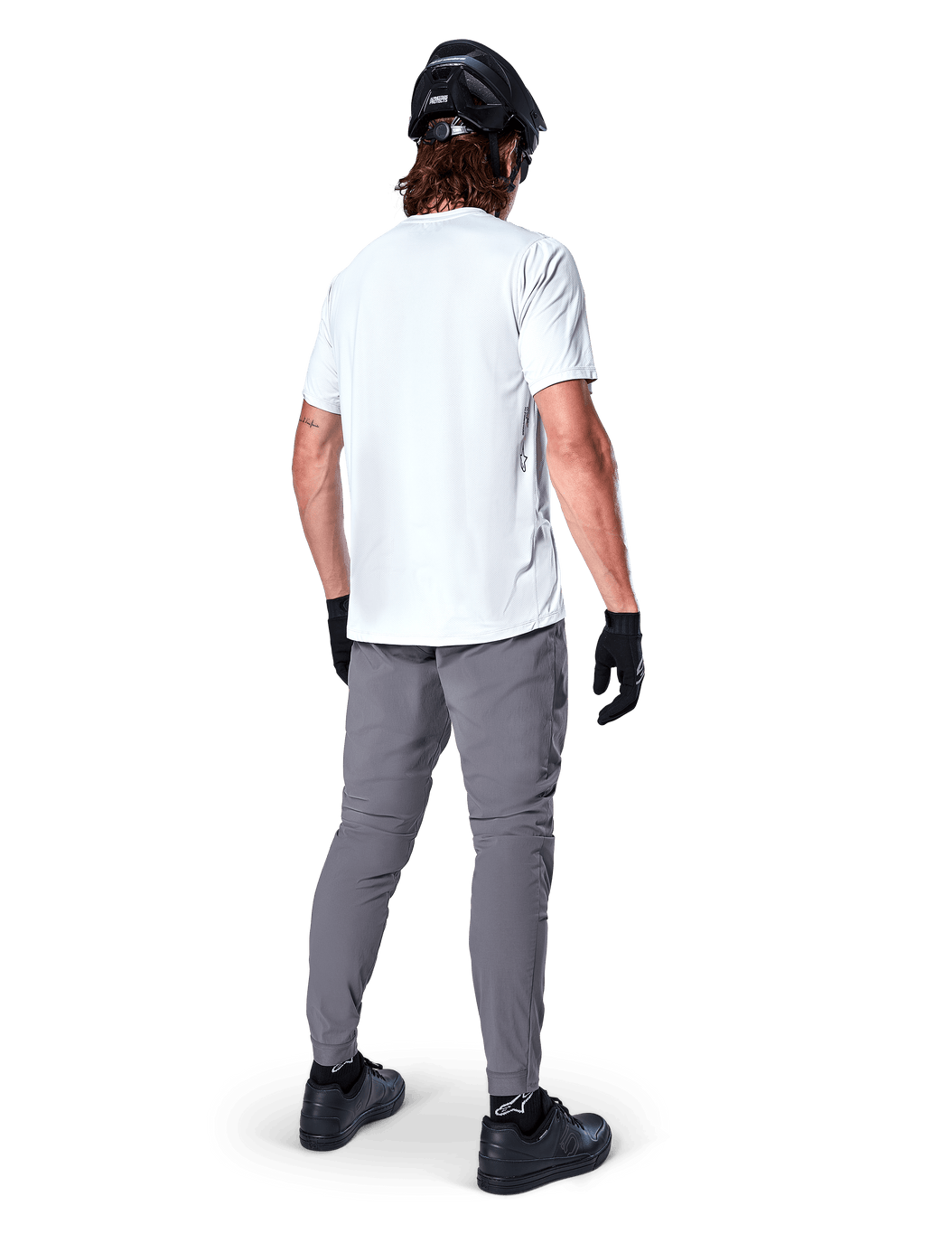 Alpinestars A-Dura bukser, mørkegrå mountainbike-bukser set bagfra, båret med en hvid kortærmet t-shirt, sort MTB-hjelm, sorte handsker og sko, regular fit-design med elastiske manchetter, holdbart off-road cykeludstyr