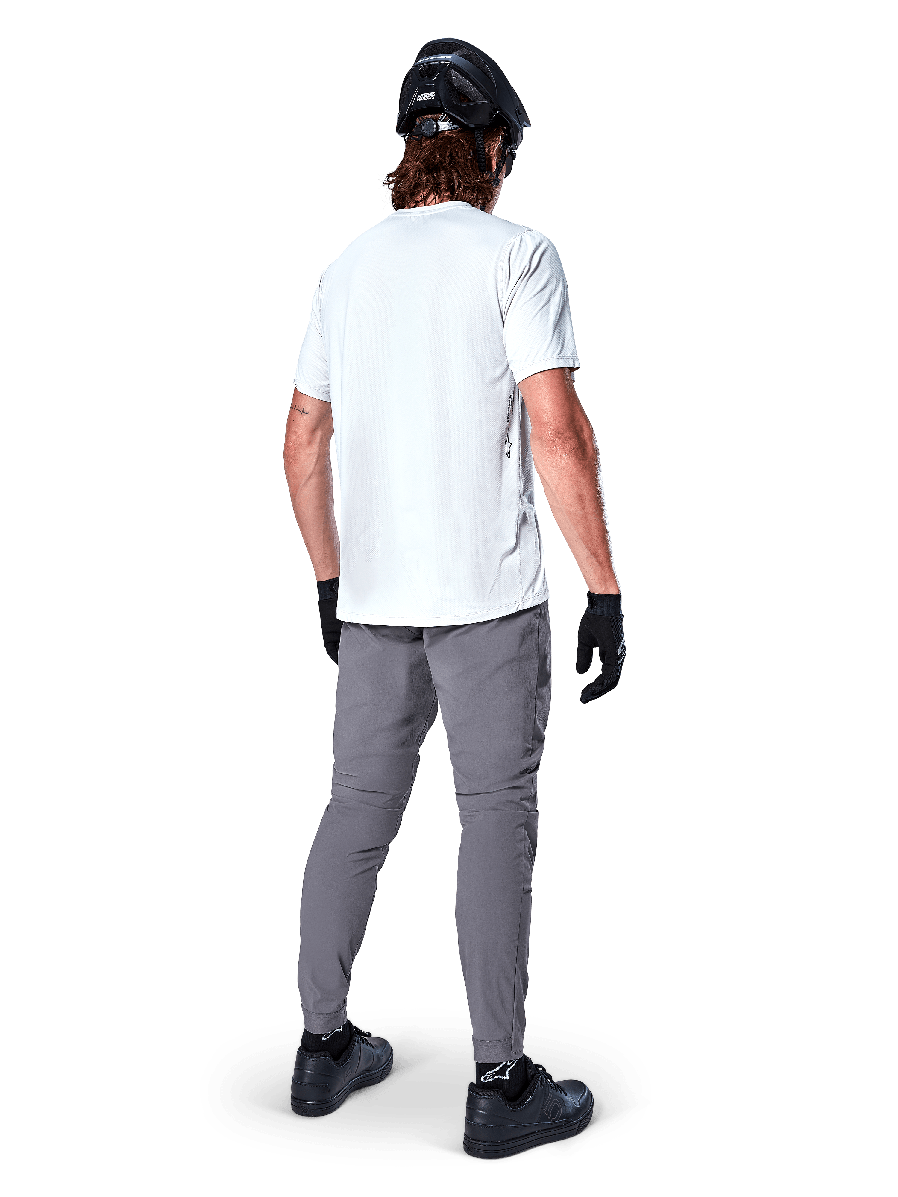 Alpinestars A-Dura bukser, mørkegrå mountainbike-bukser set bagfra, båret med en hvid kortærmet t-shirt, sort MTB-hjelm, sorte handsker og sko, regular fit-design med elastiske manchetter, holdbart off-road cykeludstyr