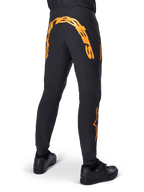 Alpinestars A-Supra Race bukser, sorte MTB-bukser, set bagfra med stort orange Alpinestars-navnetræk over bagstykket, orange logo på underbenet, performance fit med lynlåslomme, båret med sorte sko