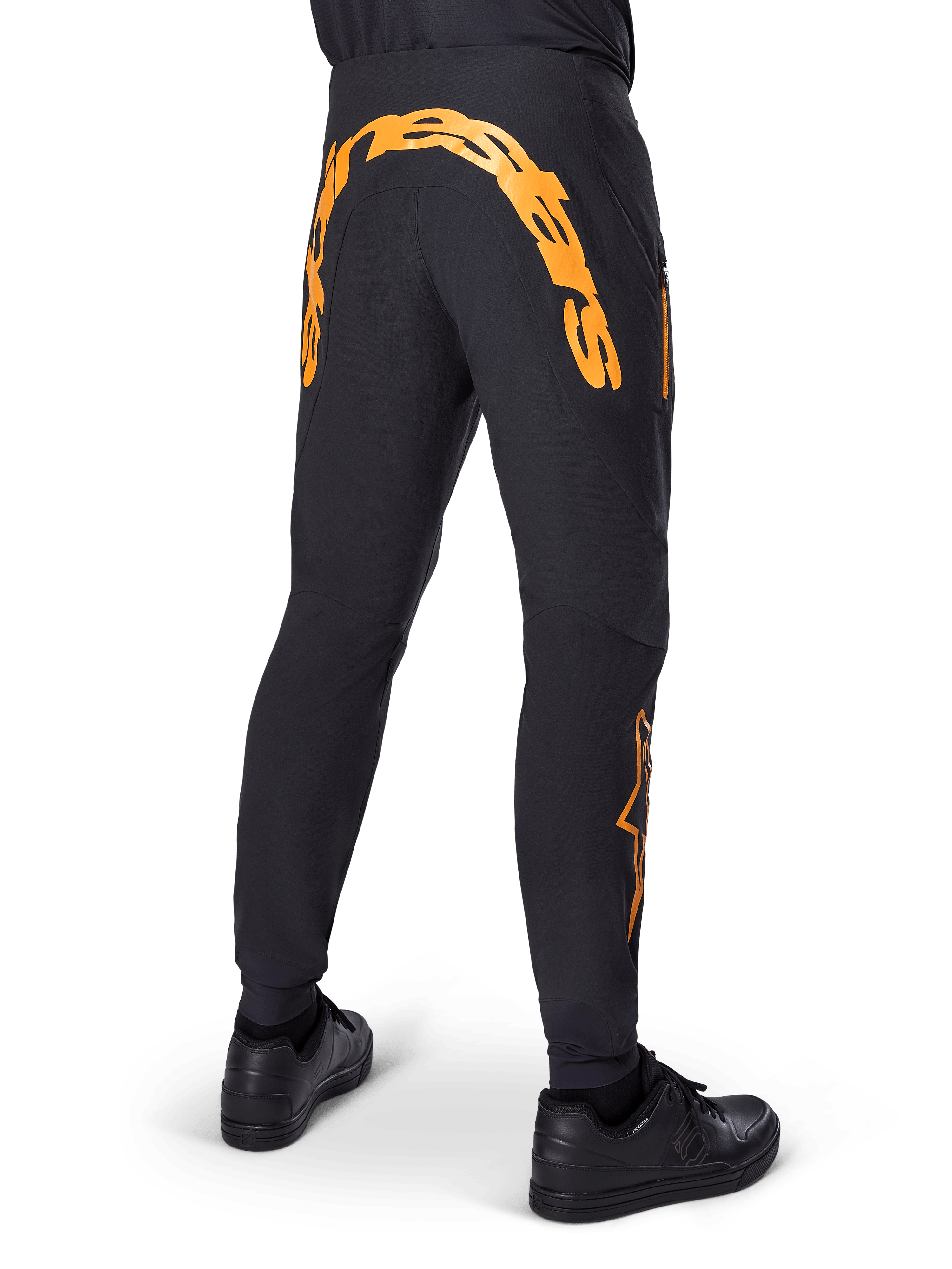 Alpinestars A-Supra Race bukser, sorte MTB-bukser, set bagfra med stort orange Alpinestars-navnetræk over bagstykket, orange logo på underbenet, performance fit med lynlåslomme, båret med sorte sko