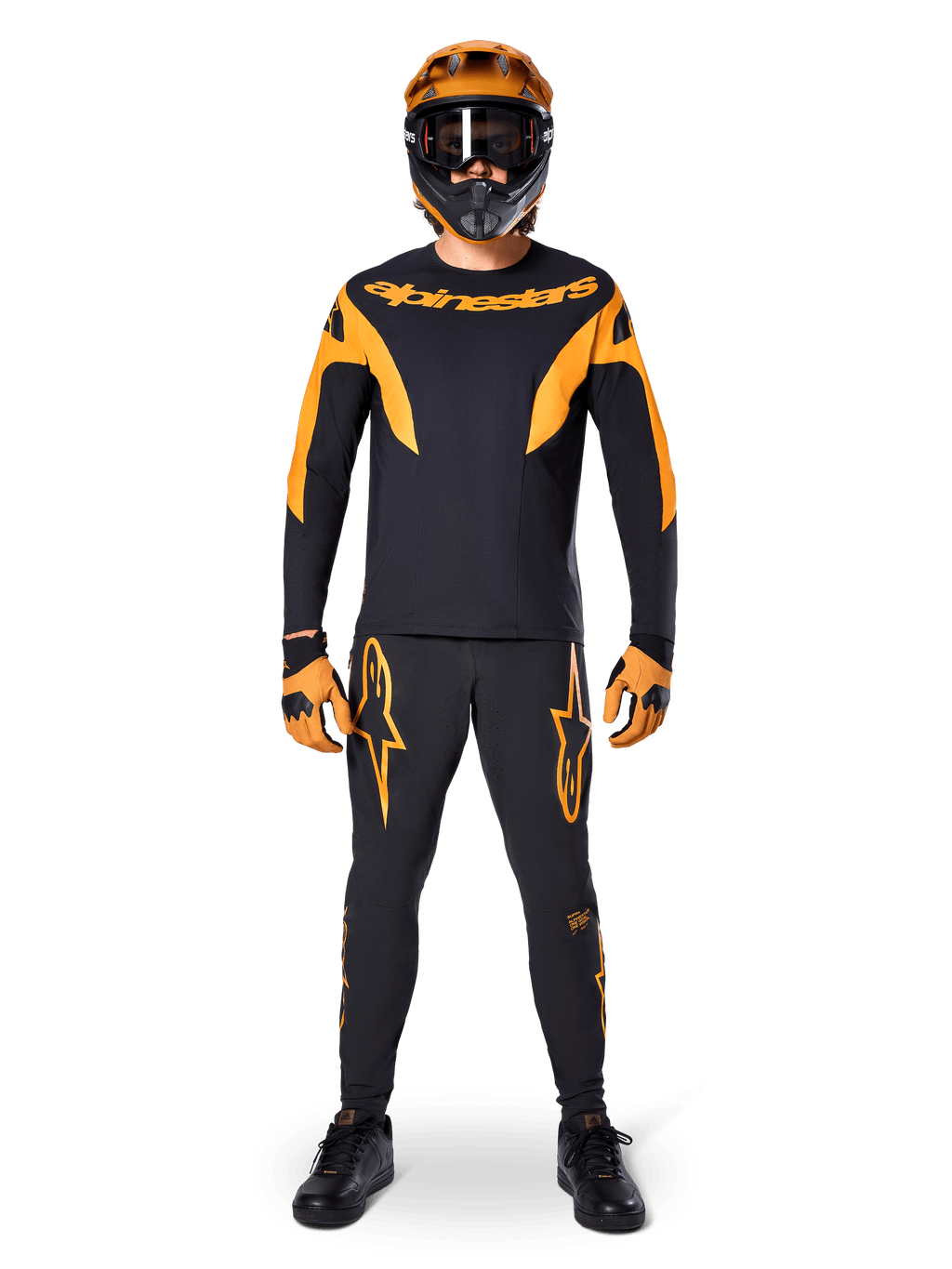 Alpinestars A-Supra Race-bukser, MTB-racerbukser, sort og orange, båret af en rytter i et komplet racersæt inklusiv en sort og orange trøje, orange hjelm og matchende handsker, med markante orange stjernelogoer på benene