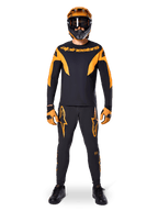 Alpinestars A-Supra Race-bukser, MTB-racerbukser, sort og orange, båret af en rytter i et komplet racersæt inklusiv en sort og orange trøje, orange hjelm og matchende handsker, med markante orange stjernelogoer på benene