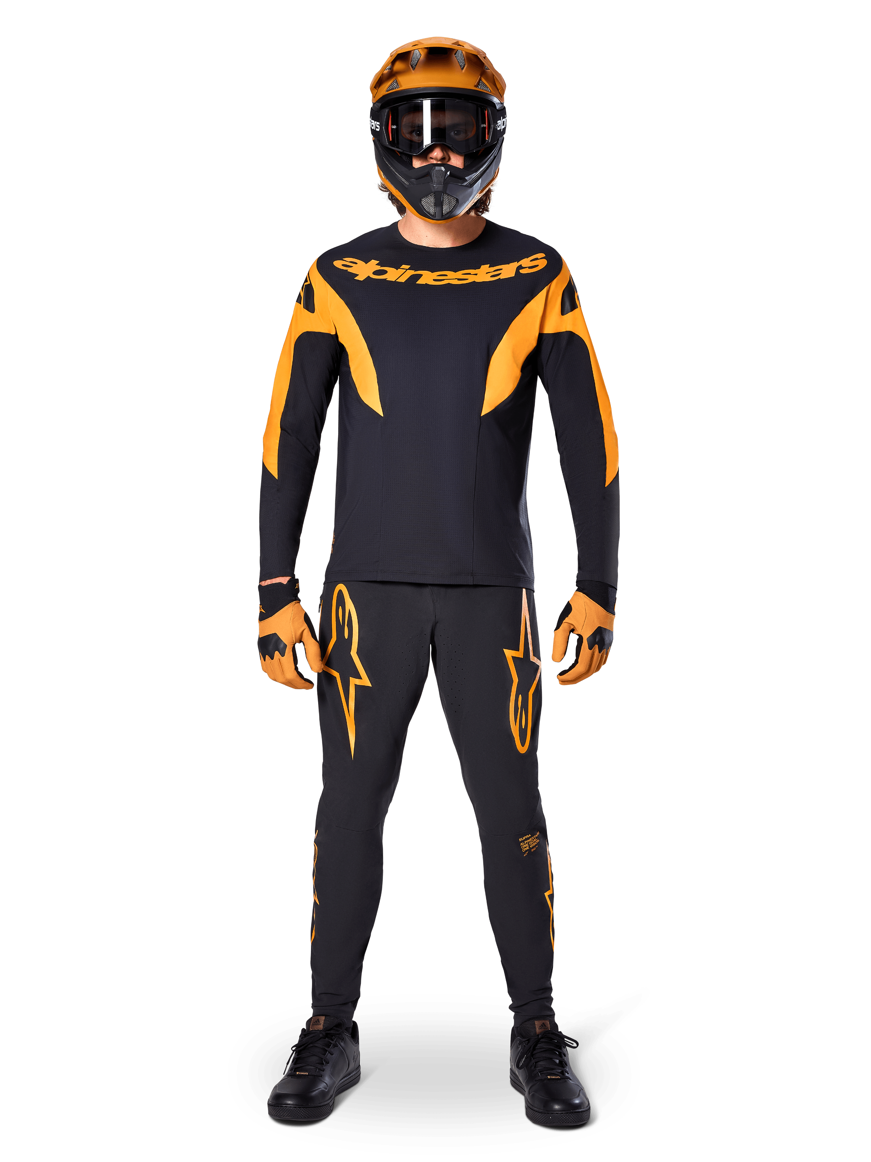 Alpinestars A-Supra Race-bukser, MTB-racerbukser, sort og orange, båret af en rytter i et komplet racersæt inklusiv en sort og orange trøje, orange hjelm og matchende handsker, med markante orange stjernelogoer på benene