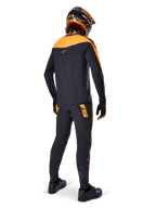 Alpinestars A-Supra Race bukser, MTB racing-bukser, sort med orange logoer, set bagfra på en rytter iført matchende sort og orange jersey, hjelm og handsker, hvilket fremhæver det MX-inspirerede ordmærke på bagstykket og en performance-pasform til tekniske spor.
