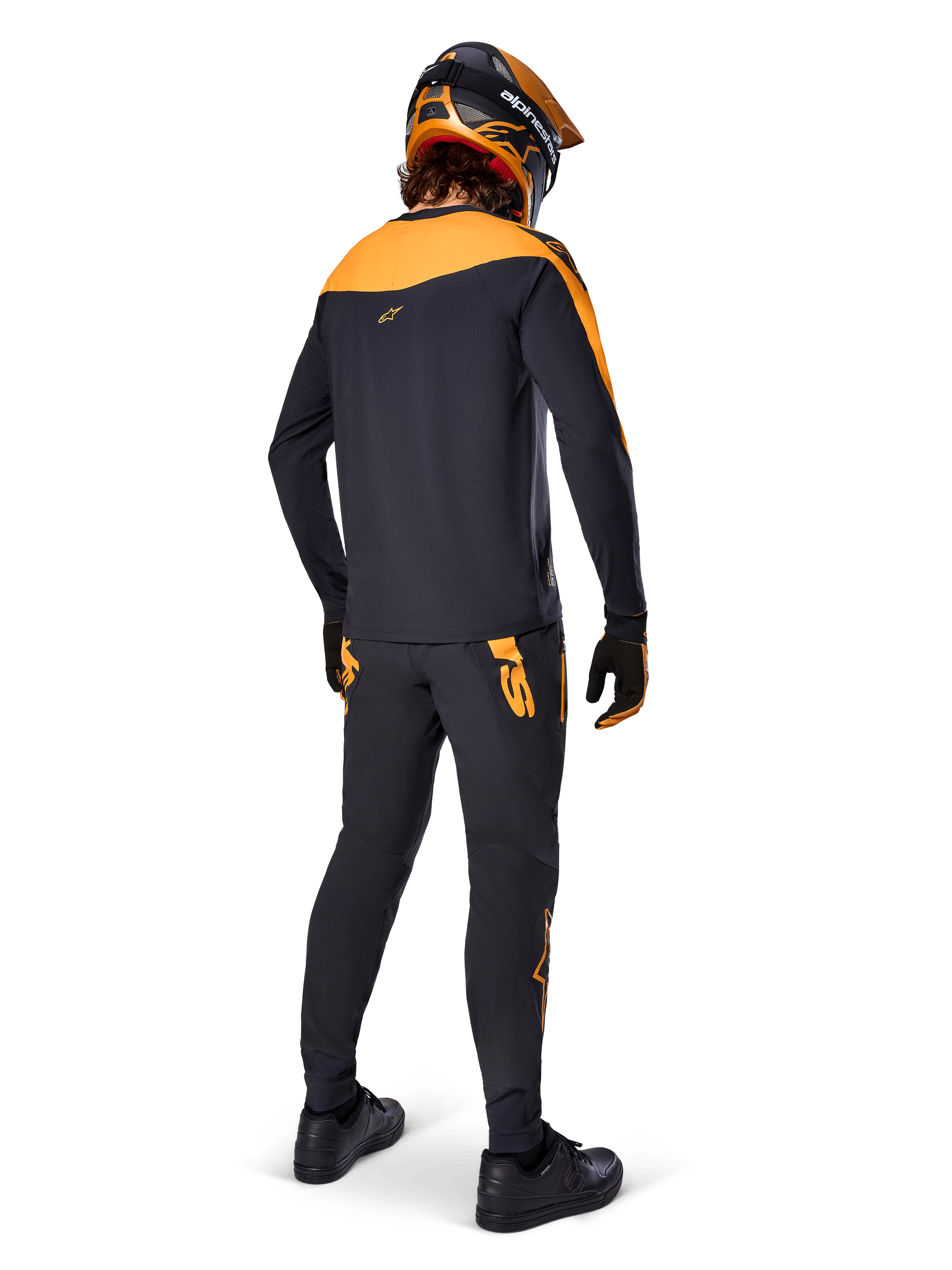 Alpinestars A-Supra Race bukser, MTB racing-bukser, sort med orange logoer, set bagfra på en rytter iført matchende sort og orange jersey, hjelm og handsker, hvilket fremhæver det MX-inspirerede ordmærke på bagstykket og en performance-pasform til tekniske spor.